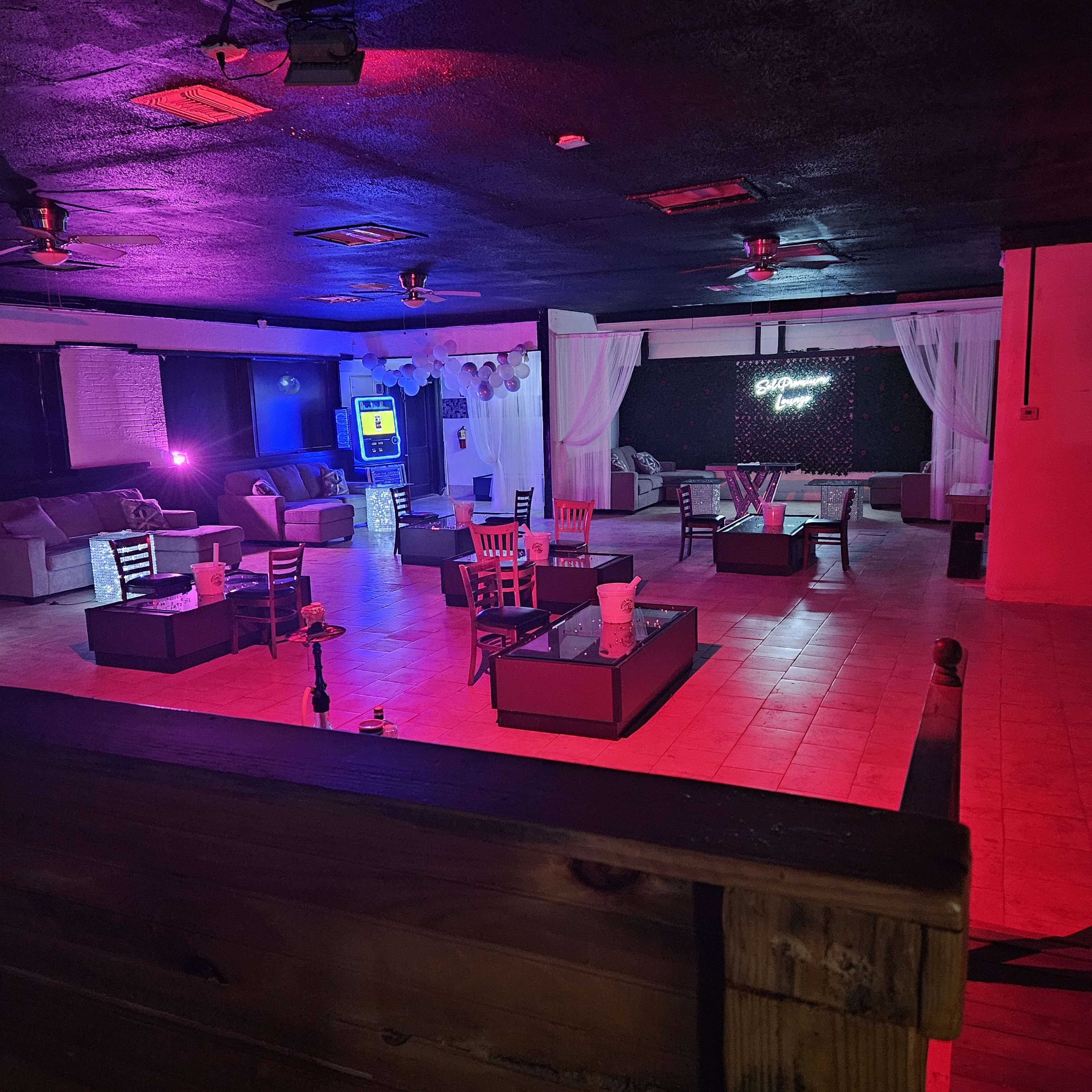 An empty lounge with seating arrangements, colorful lighting, and a bar area.