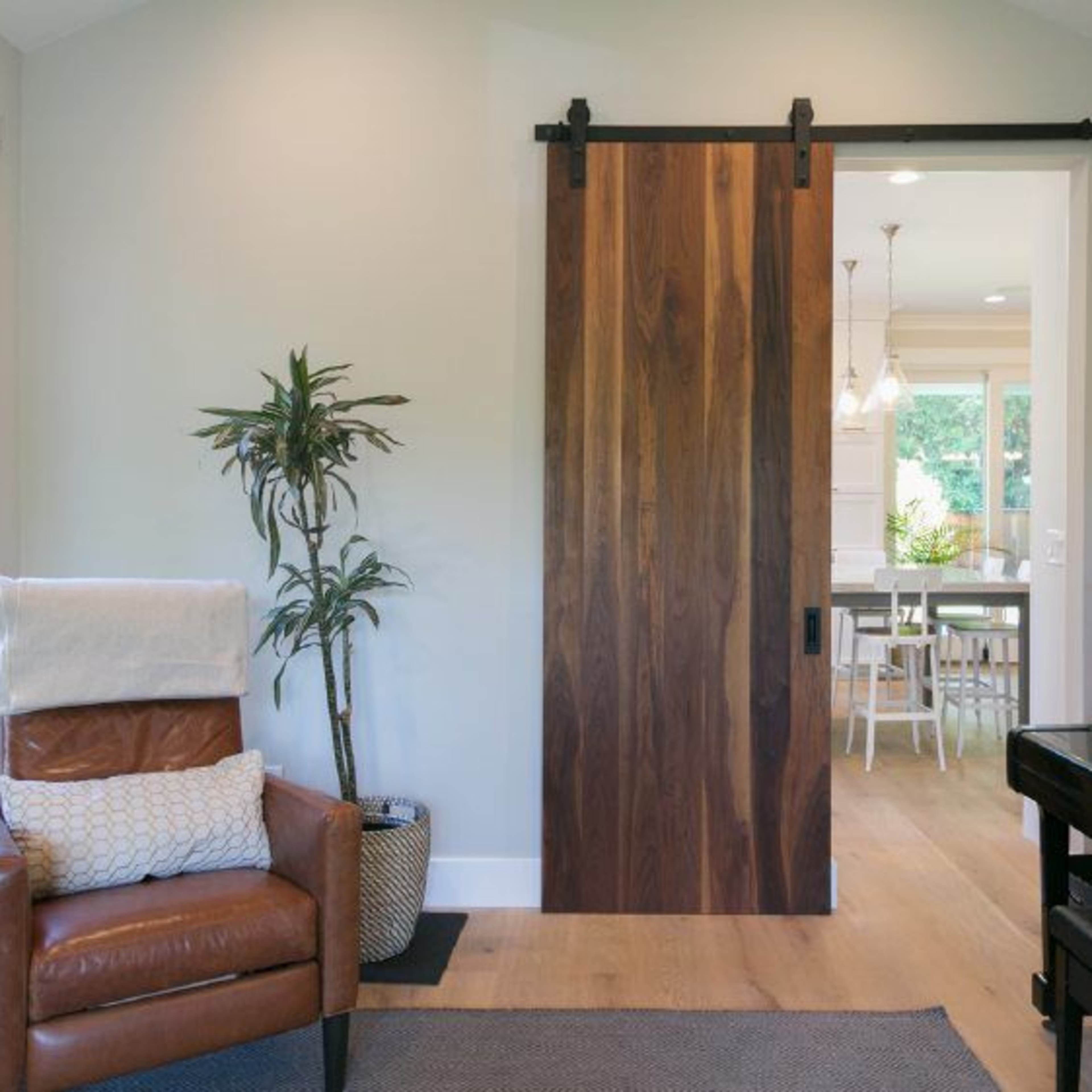 A cozy interior with a brown leather chair, a sliding wooden door, and a piano next to a large window.