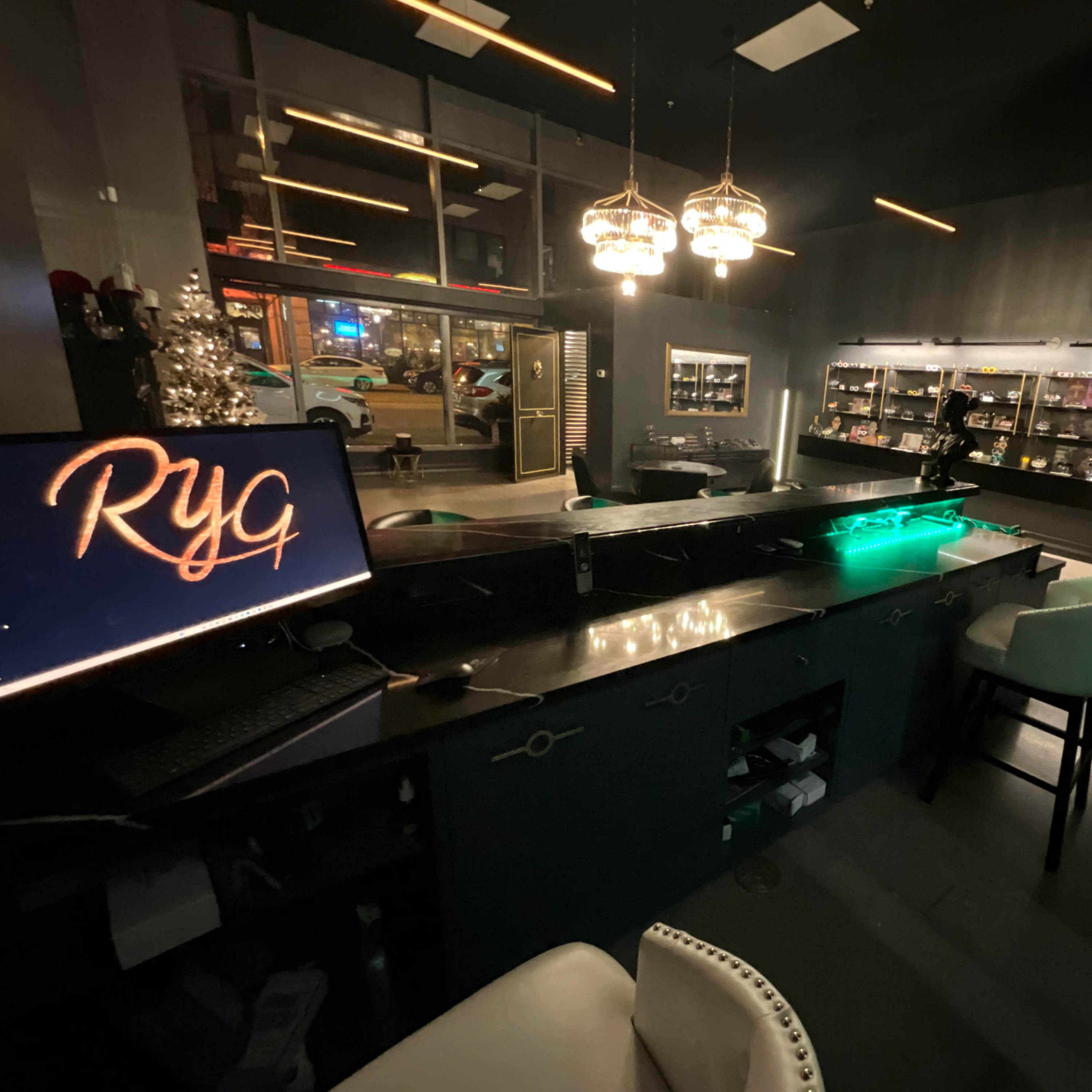 A dimly lit modern bar area with a sleek counter, illuminated by pendant lights, and shelves displaying various items in the background.