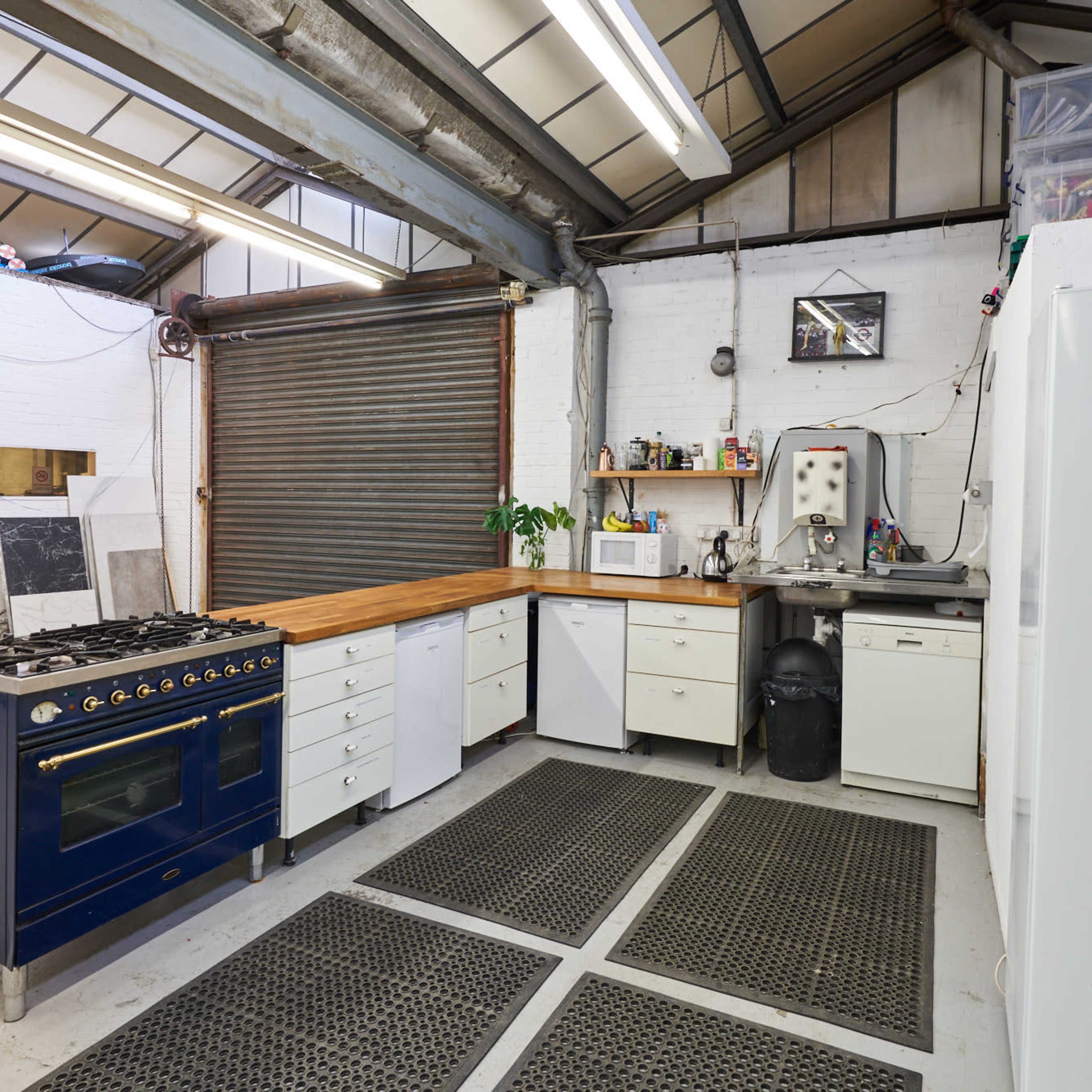 A kitchen area with a gas stove, a refrigerator, and a combination of countertop and cabinets in a warehouse-like environment.