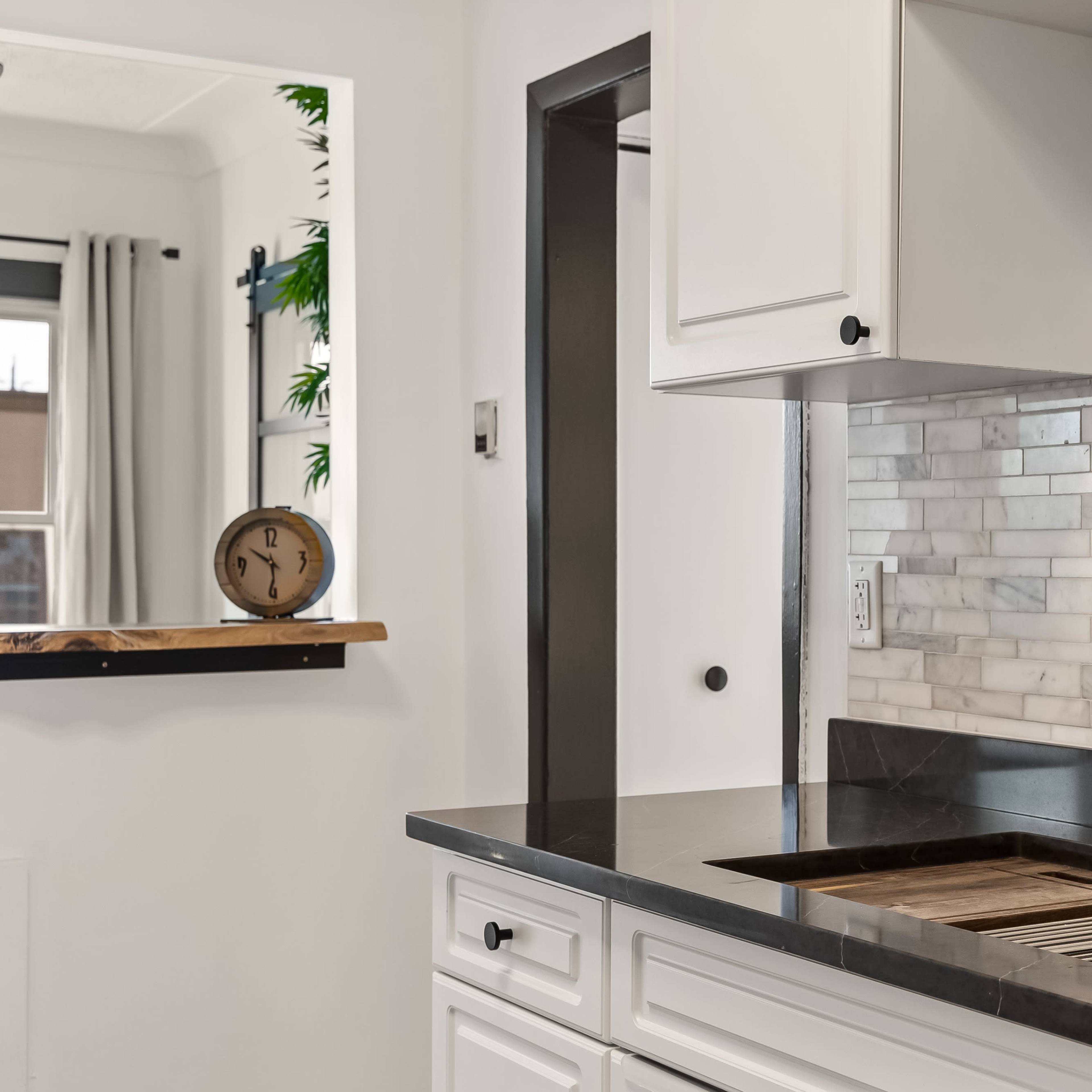 A modern kitchen with a black countertop, a stainless steel faucet, and a backsplash made of white marble tiles.