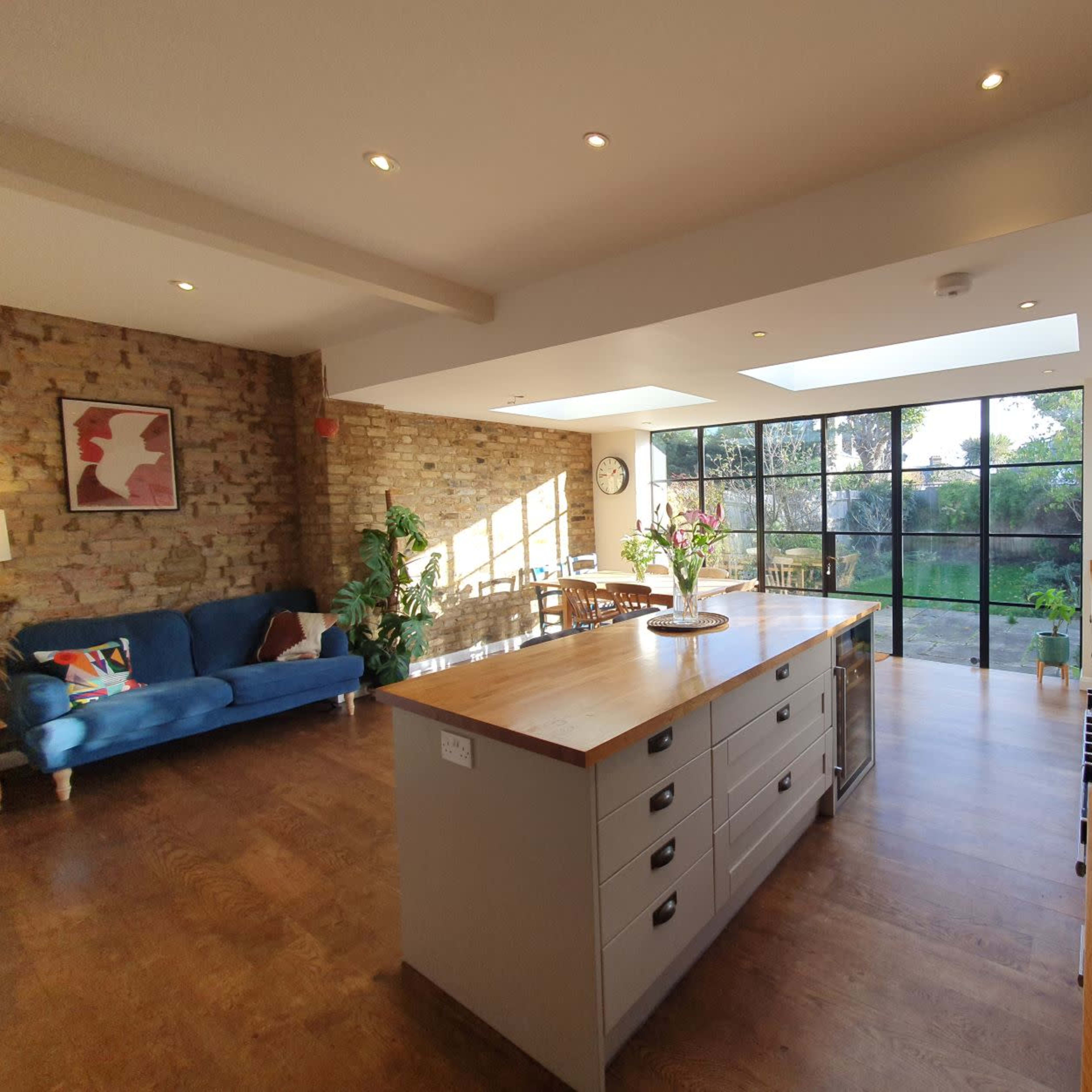 A modern kitchen with a wooden island, a gas stove, and large windows overlooking a garden.