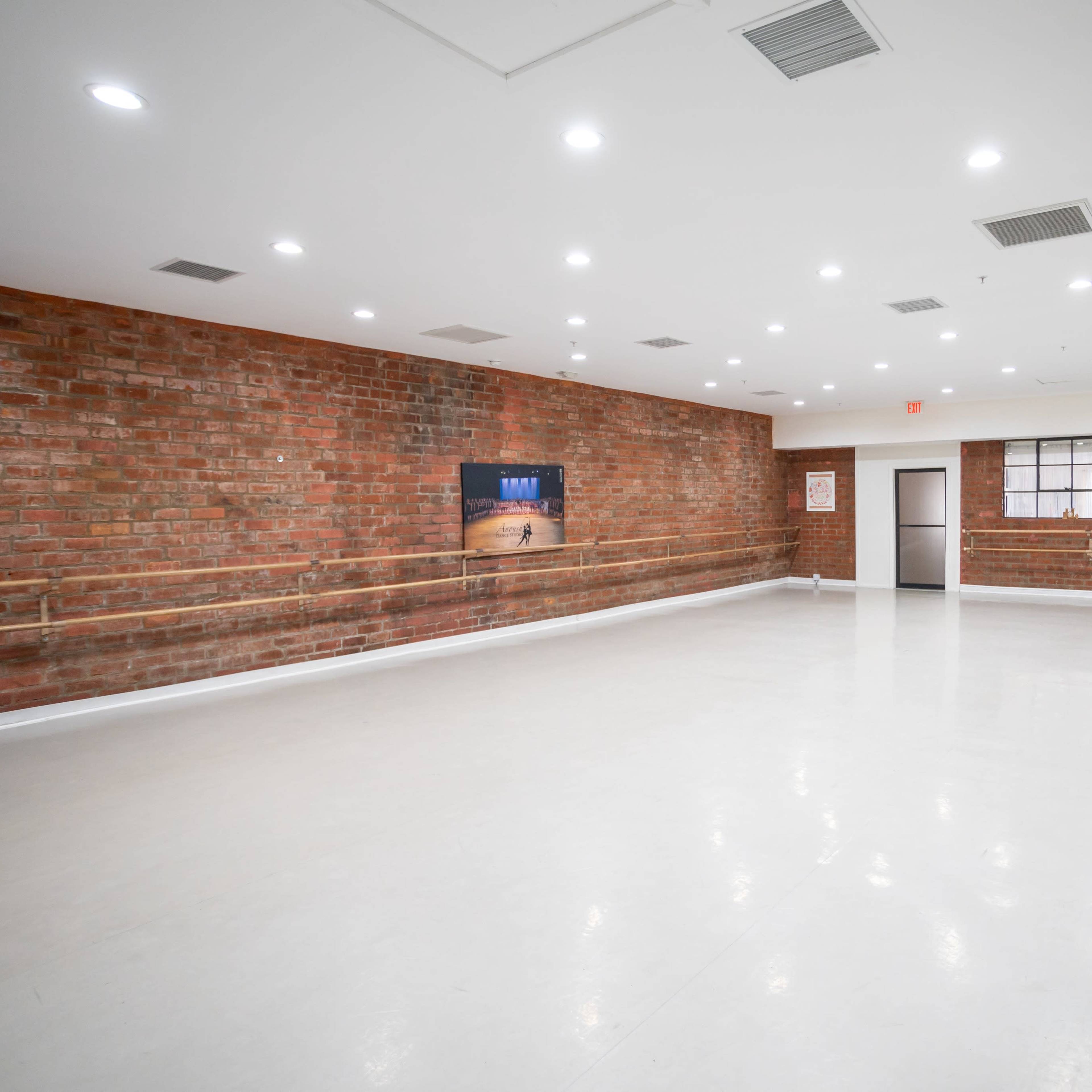A spacious, empty dance studio with exposed brick walls and a large mirror.