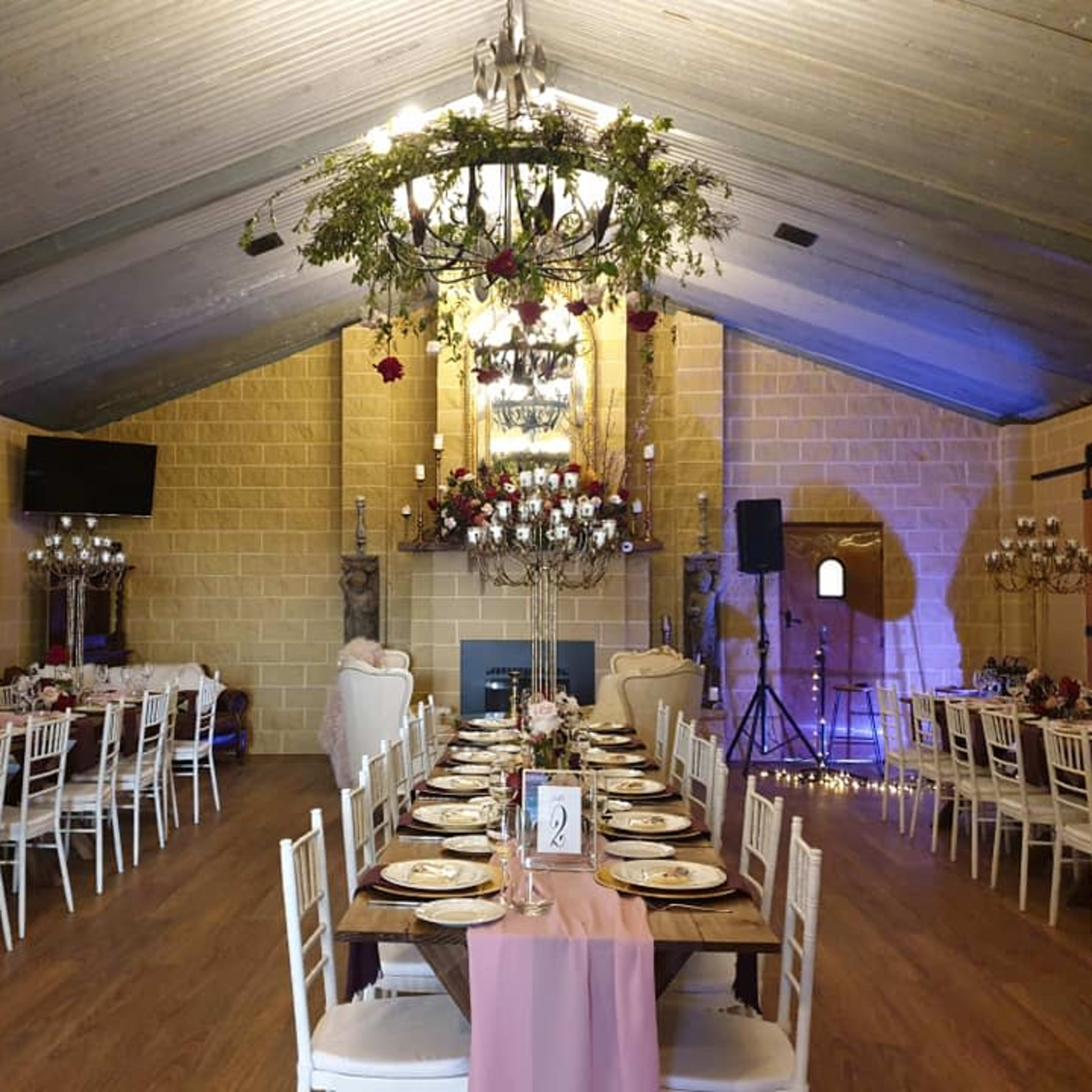 A banquet hall decorated with long tables set for dining, featuring floral centerpieces and chandeliers hanging from the vaulted ceiling.