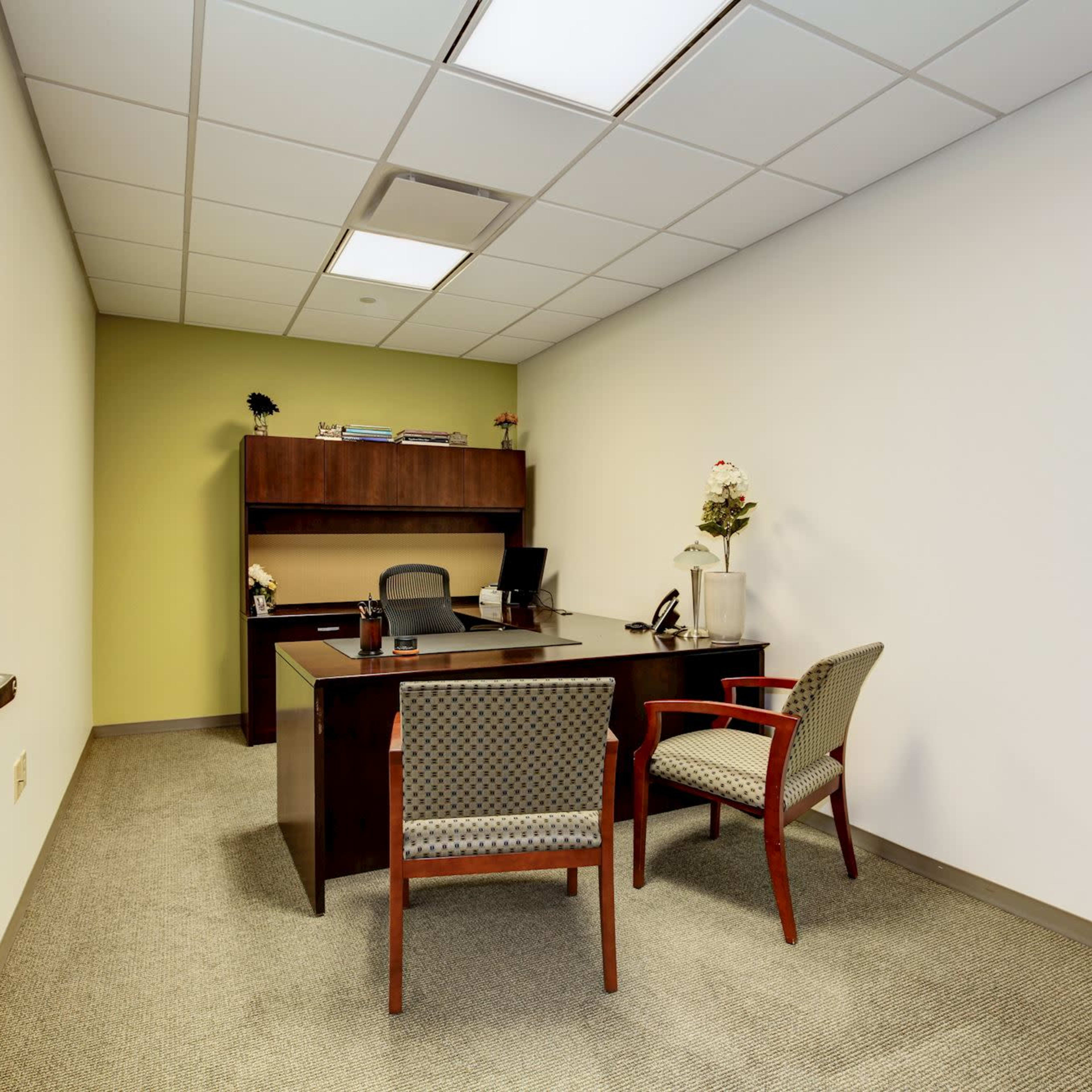 A small office with a desk, two chairs, and a shelf against a wall.