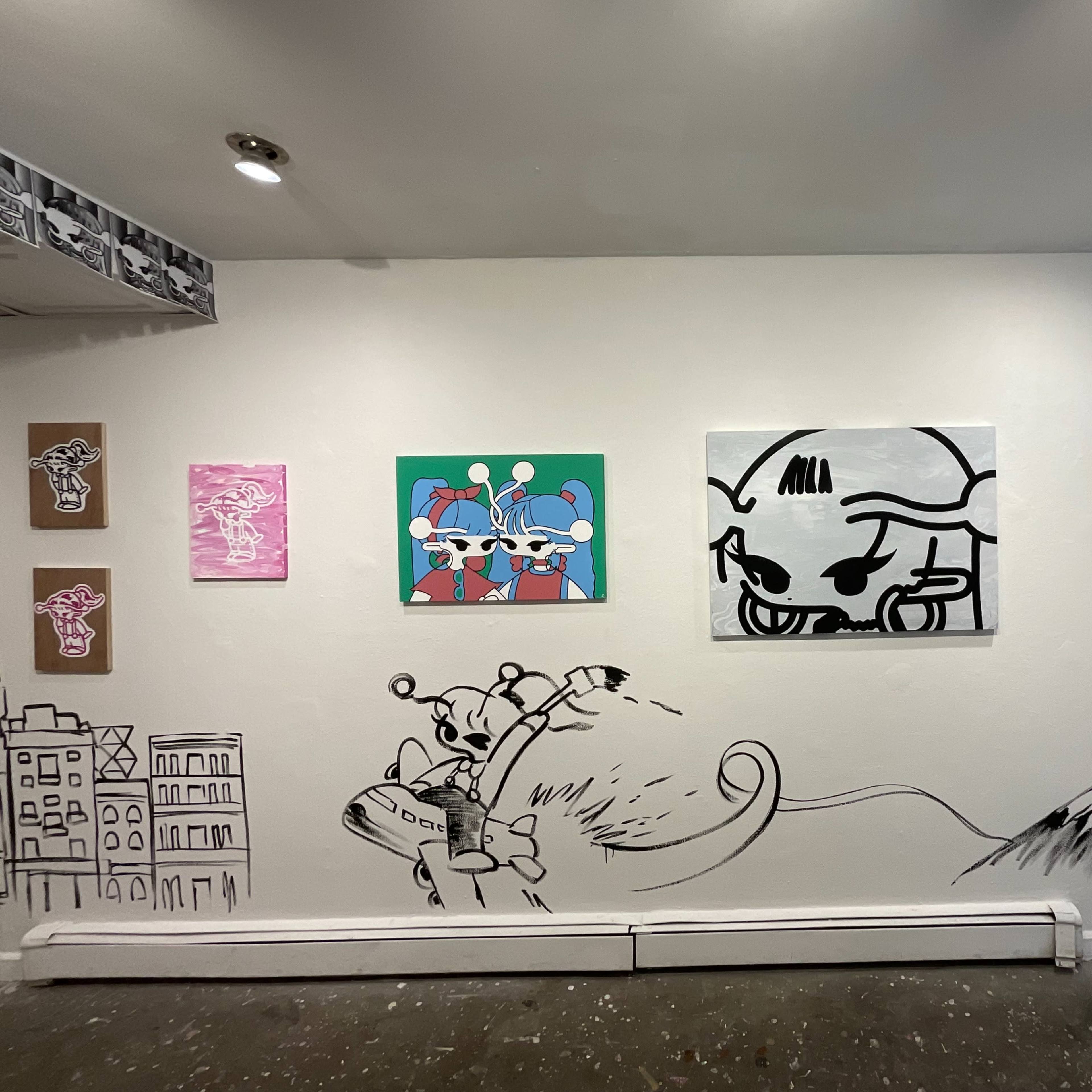 An art gallery wall featuring various colorful artworks, including framed paintings and a large mural depicting characters and landscapes.