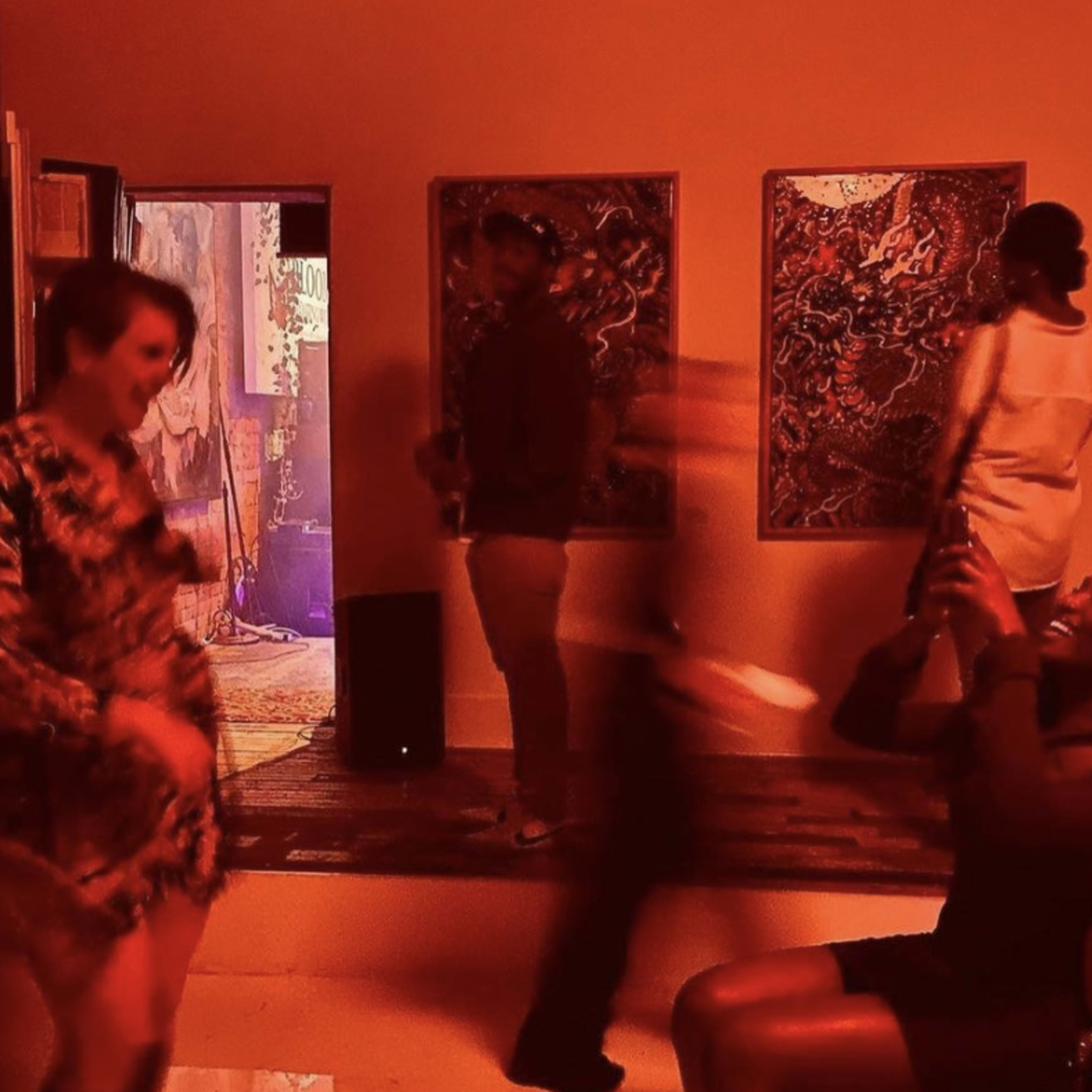People socialize in a dimly lit room adorned with colorful artwork.