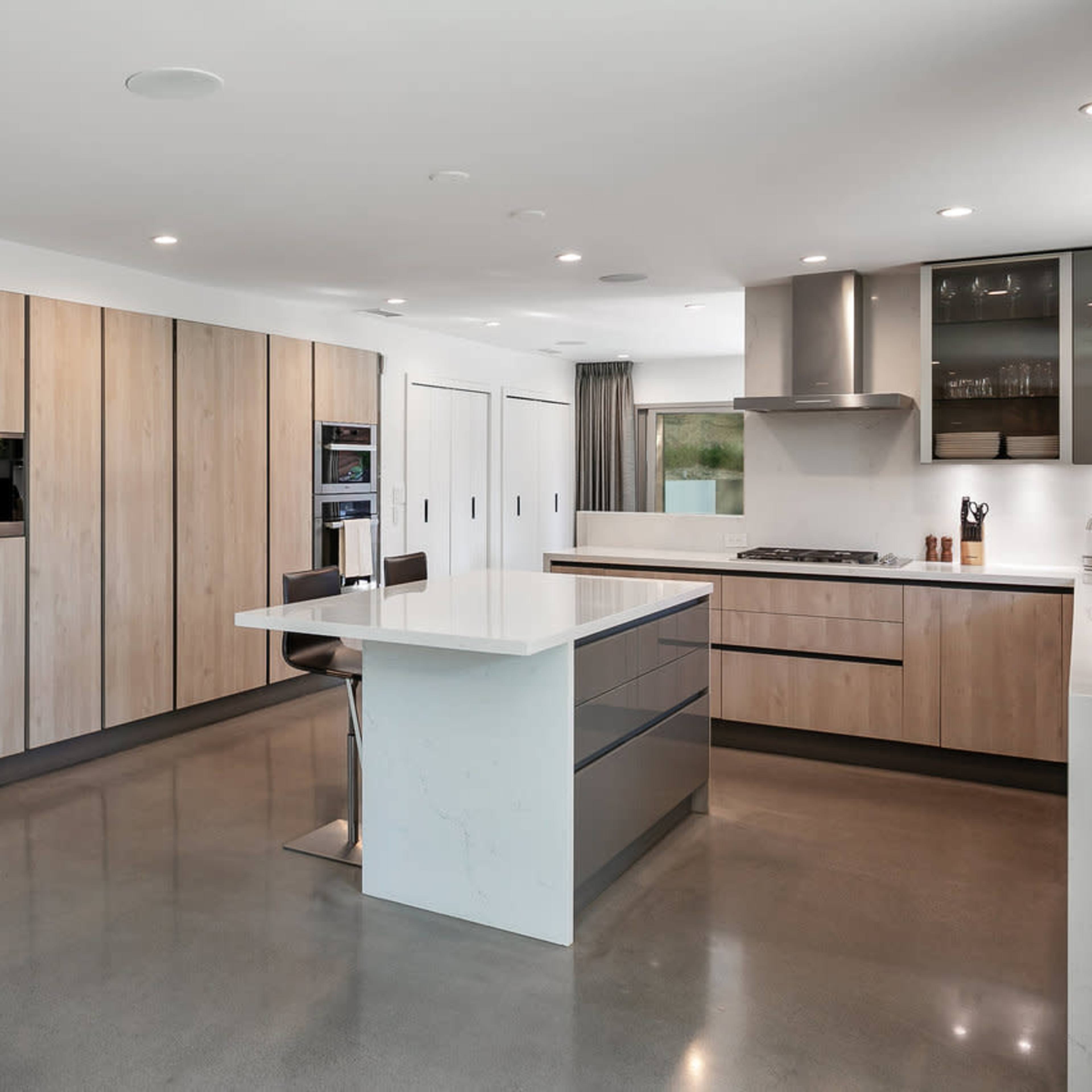 A modern kitchen featuring wood cabinetry, a central island with a white countertop, and stainless steel appliances.