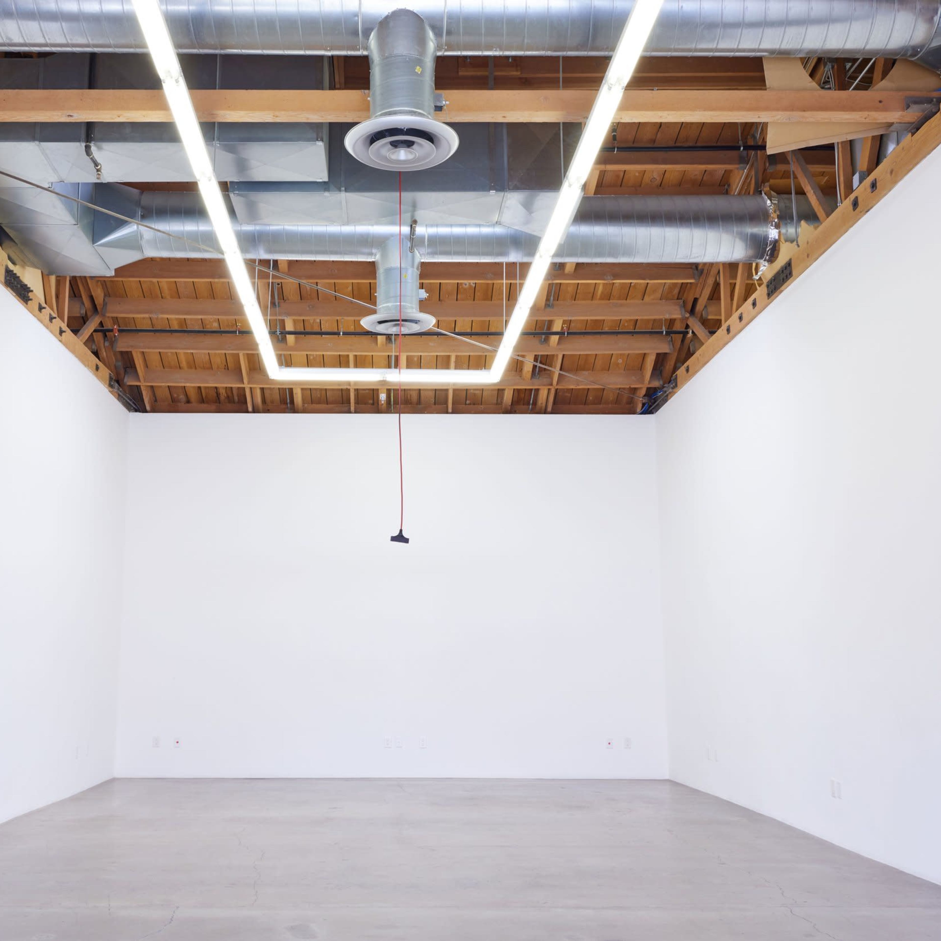 An empty, well-lit room with a high wooden ceiling, exposed ventilation ducts, and a minimalistic design.