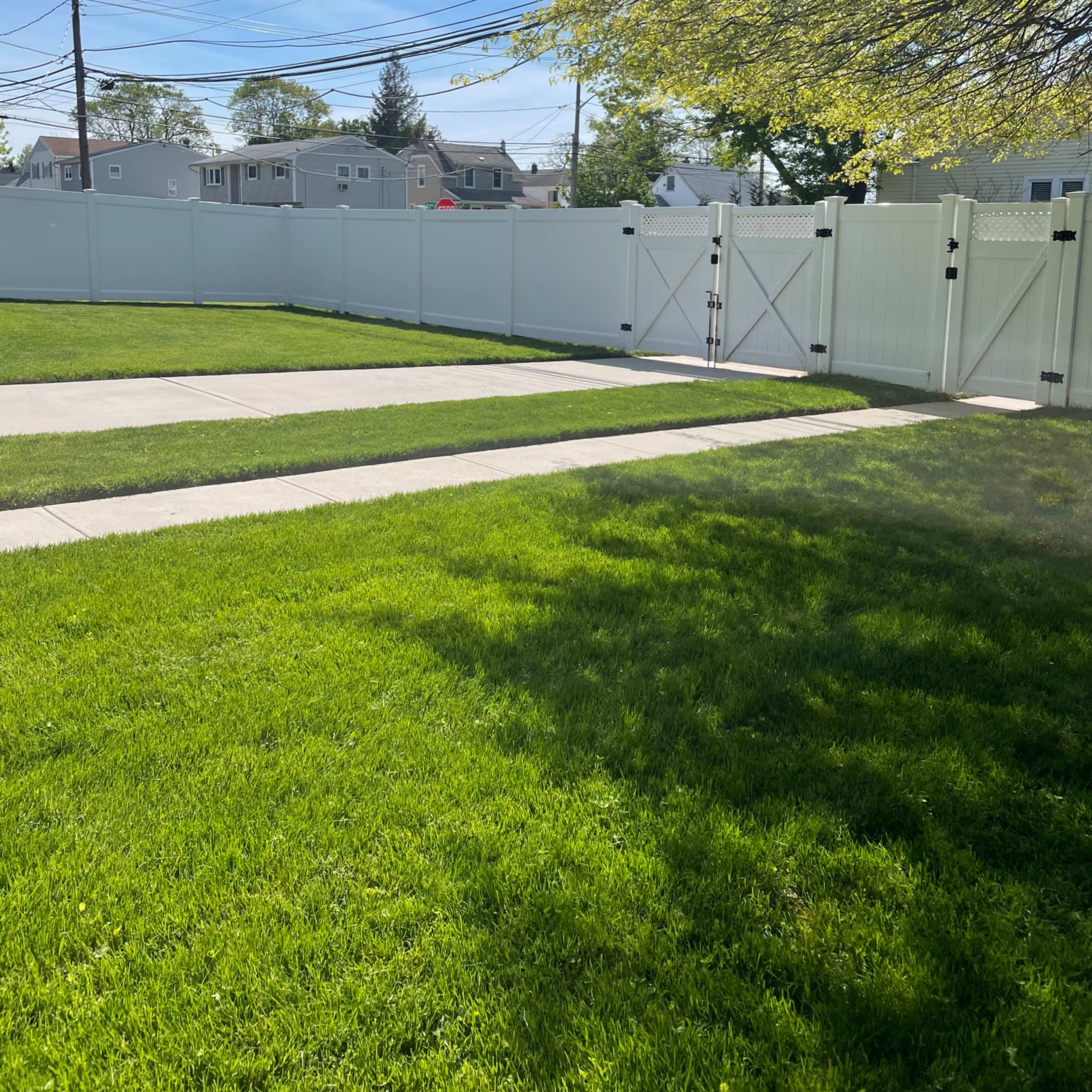 A well-maintained lawn with two paths leading to a white fence and gate under a clear blue sky.