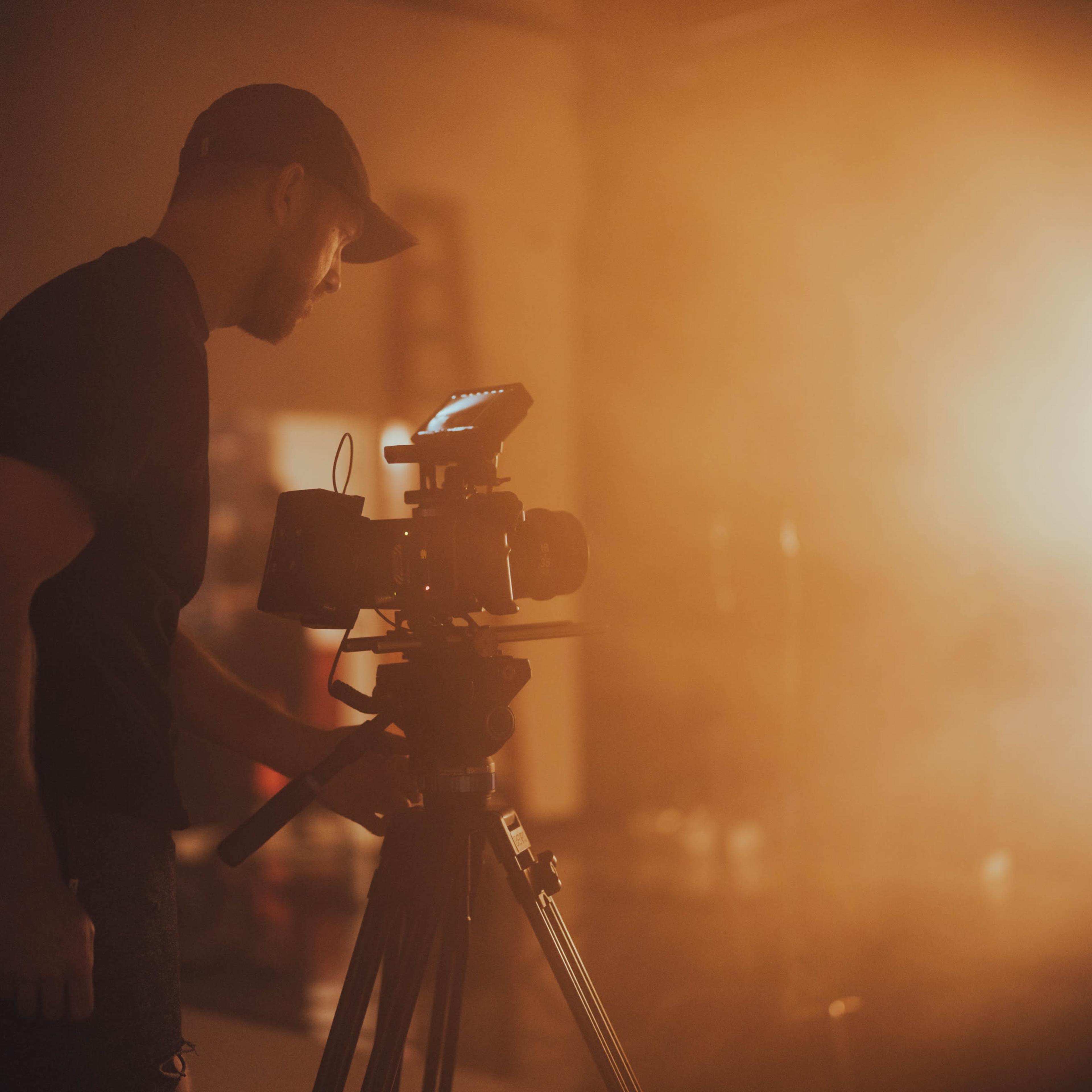 A person is adjusting a camera on a tripod in a dimly lit studio.