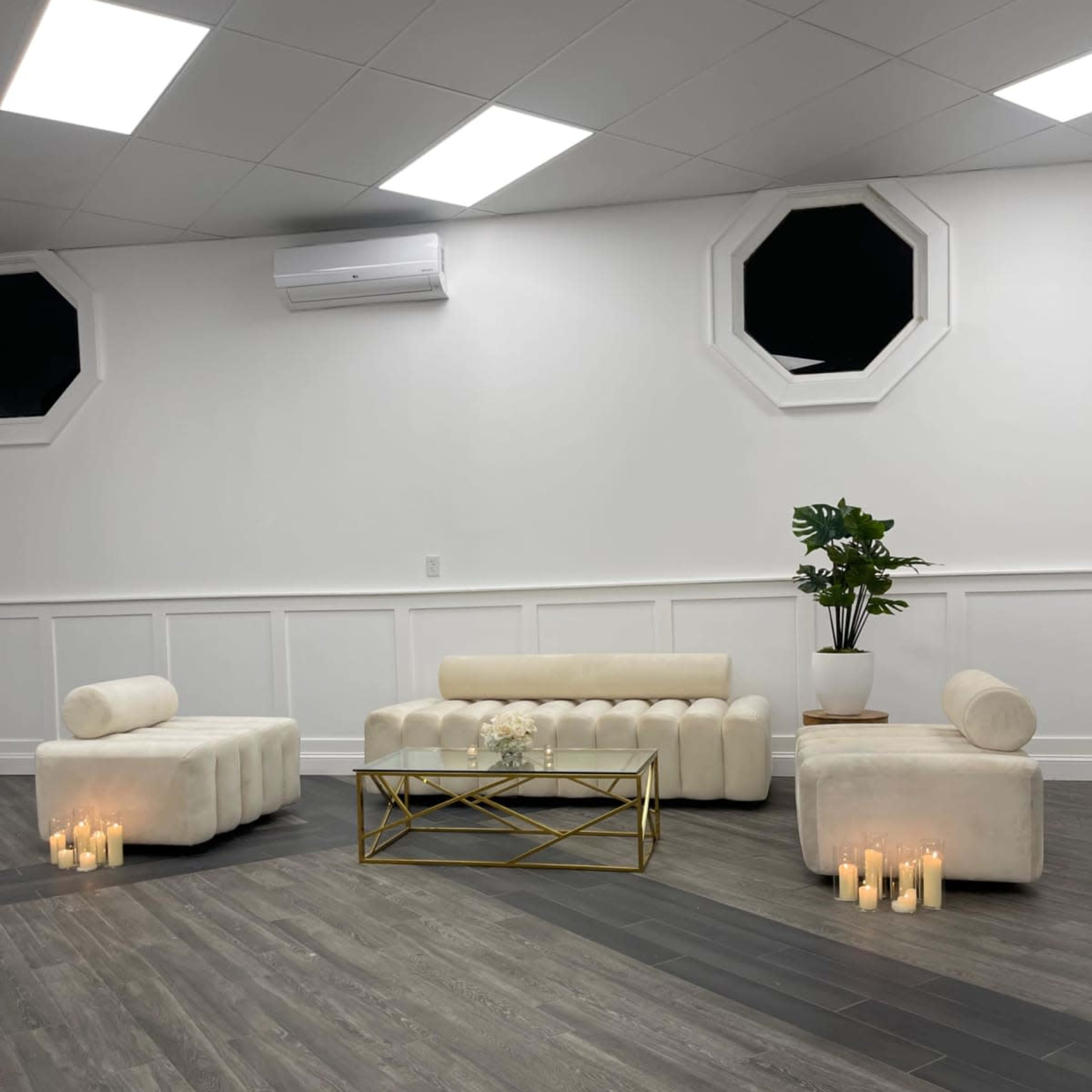 A spacious room features white seating arrangements and a gold coffee table, illuminated by candles on the floor.