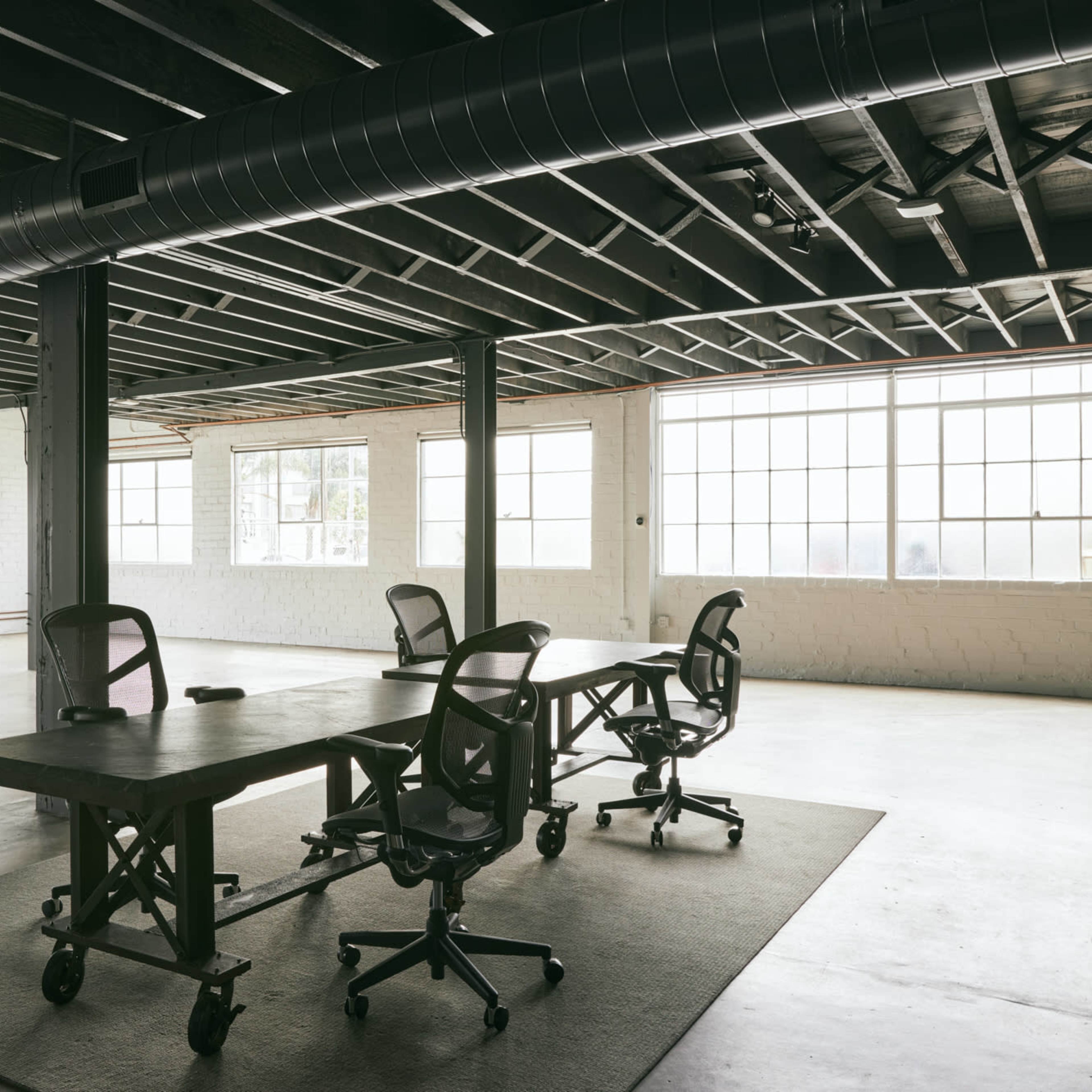 A spacious office features several workstations with rolling chairs and large windows allowing ample natural light.