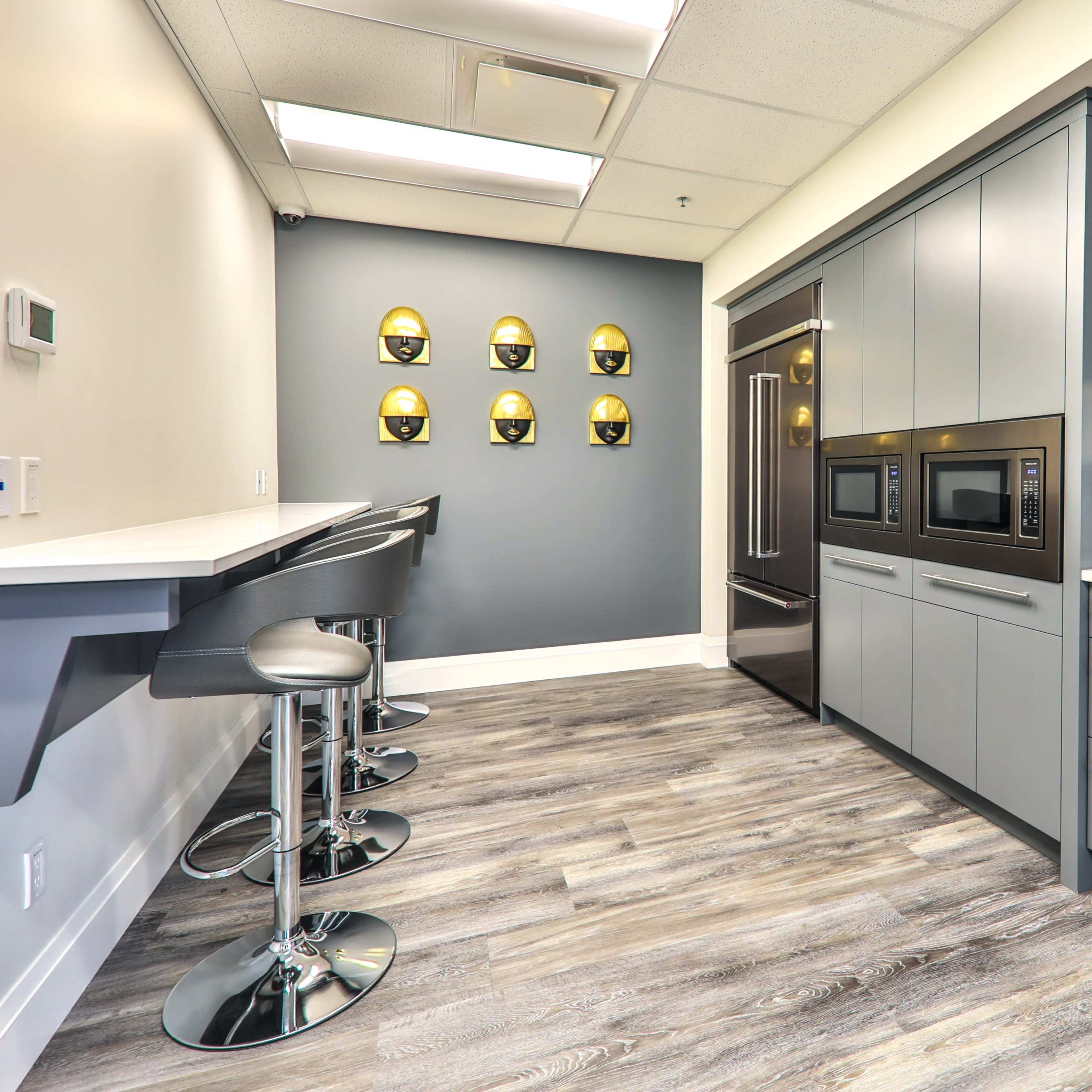 A modern kitchen with gray cabinetry, stainless steel appliances, and a sleek countertop, featuring a bar area with high stools.