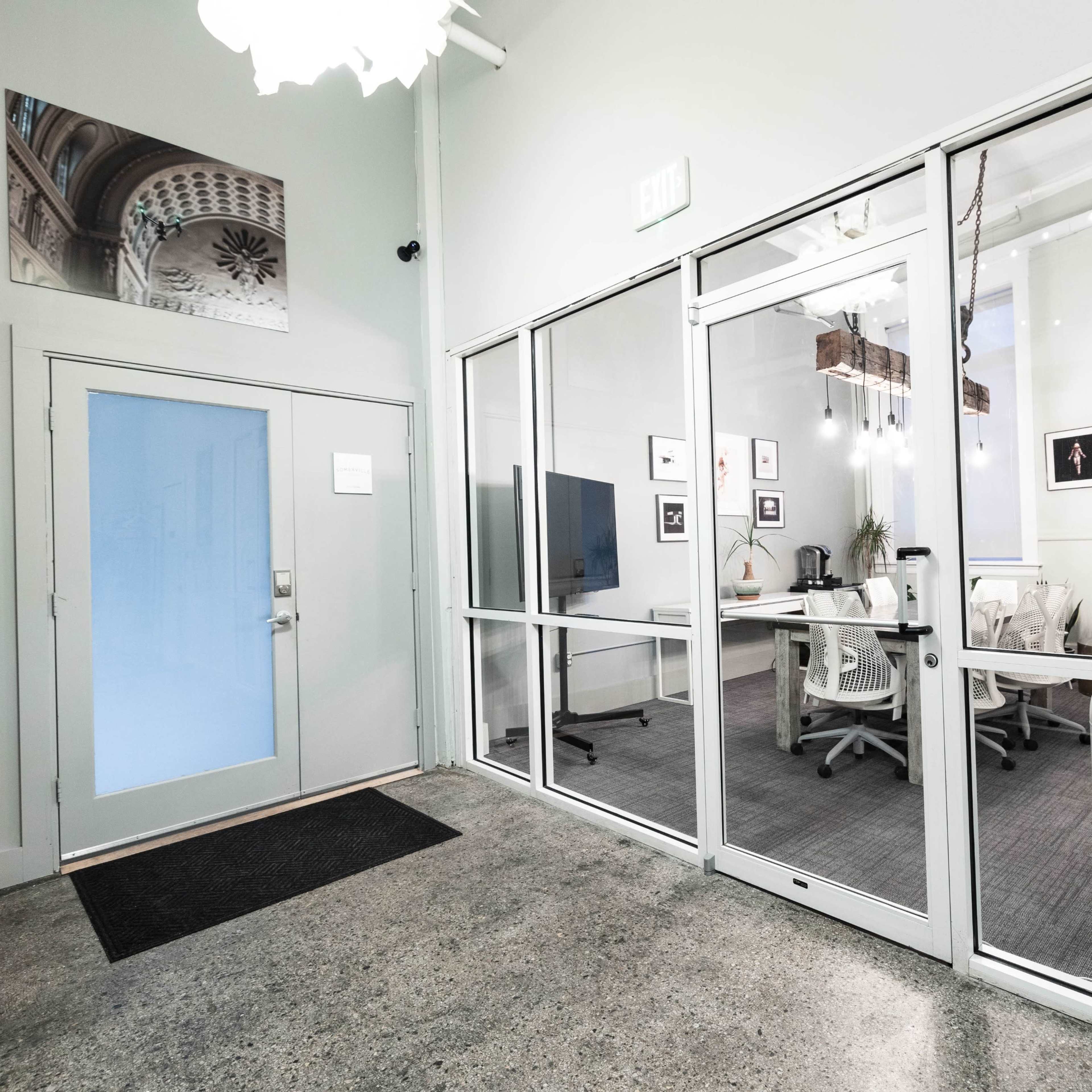 A modern office entrance with a glass-walled meeting room visible through a large window.