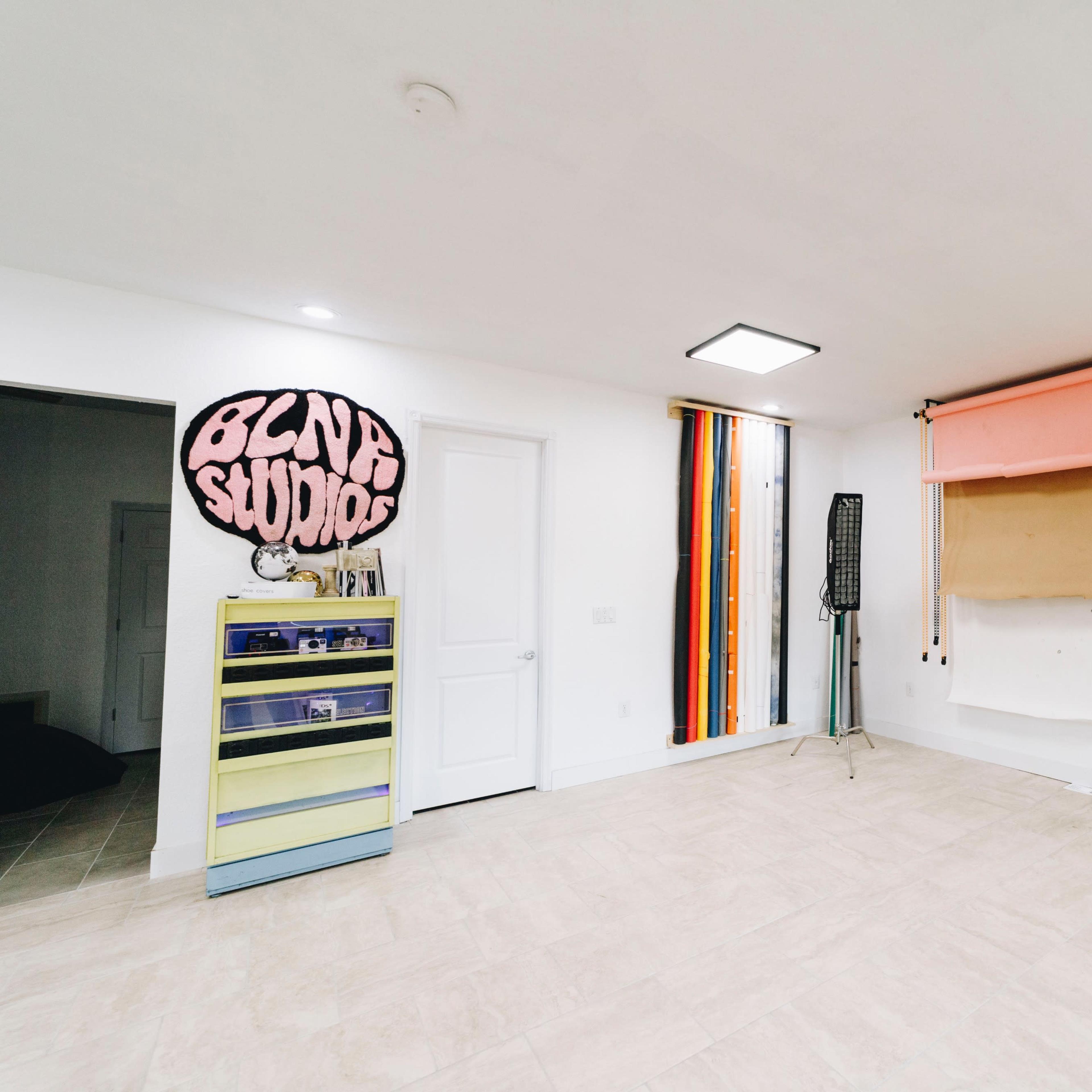 A spacious room with a white floor and walls, featuring a colorful backdrop, a tall light stand, and storage cabinets.