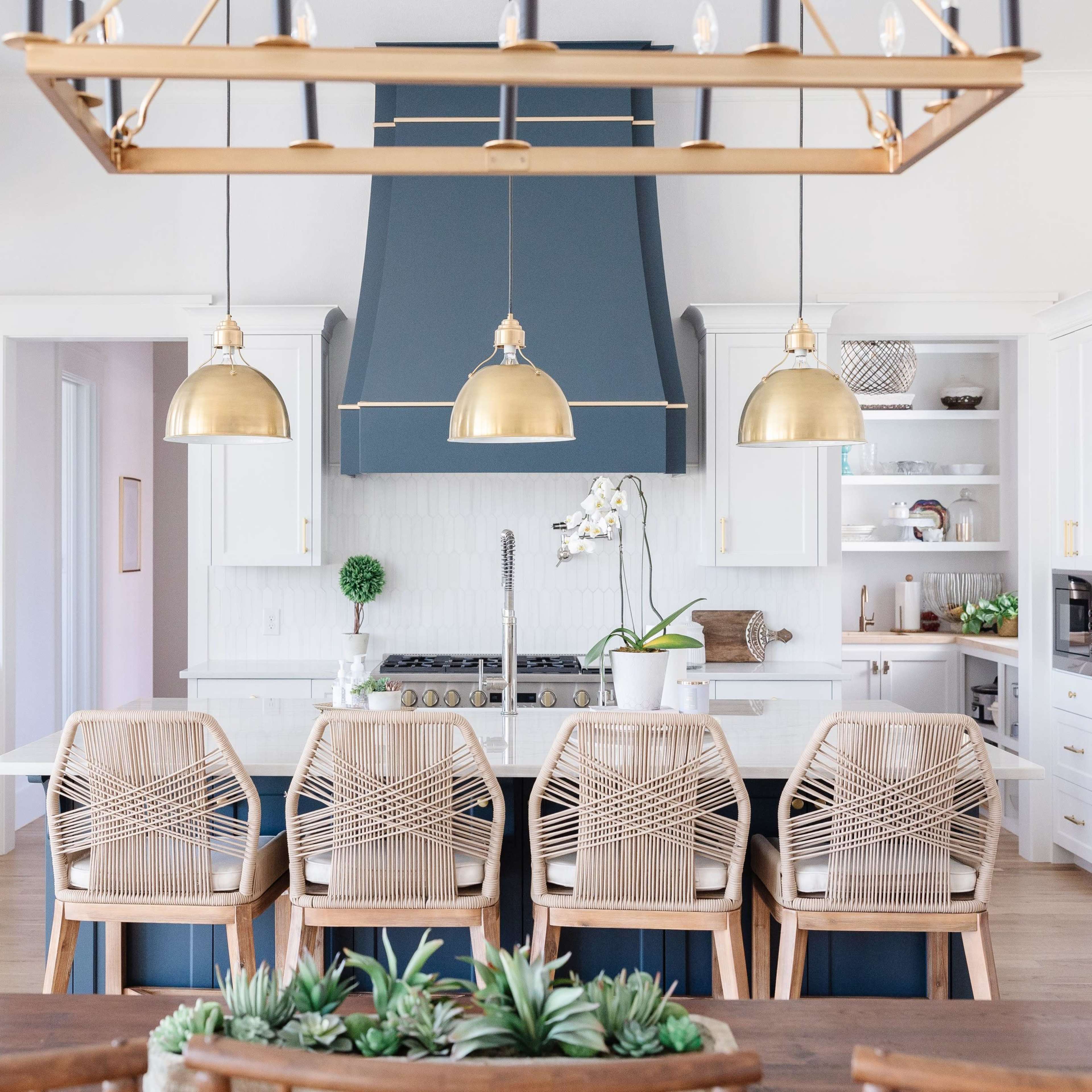A modern kitchen features a large island with a gas stove, surrounded by six wooden seats and pendant lights above.