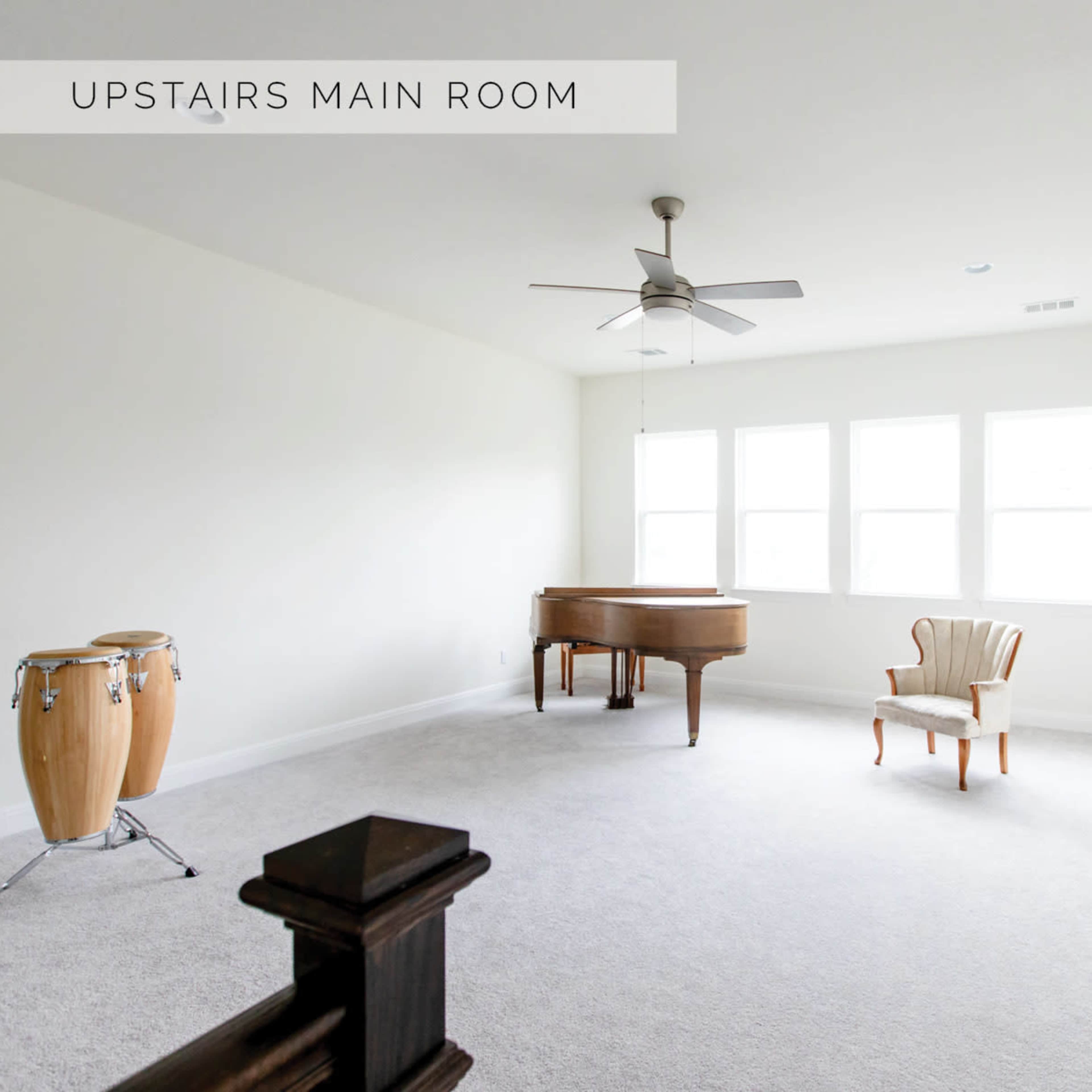 The room features a grand piano, a chair, a stool, conga drums, and three windows, all set against a neutral-colored wall and carpeted floor.