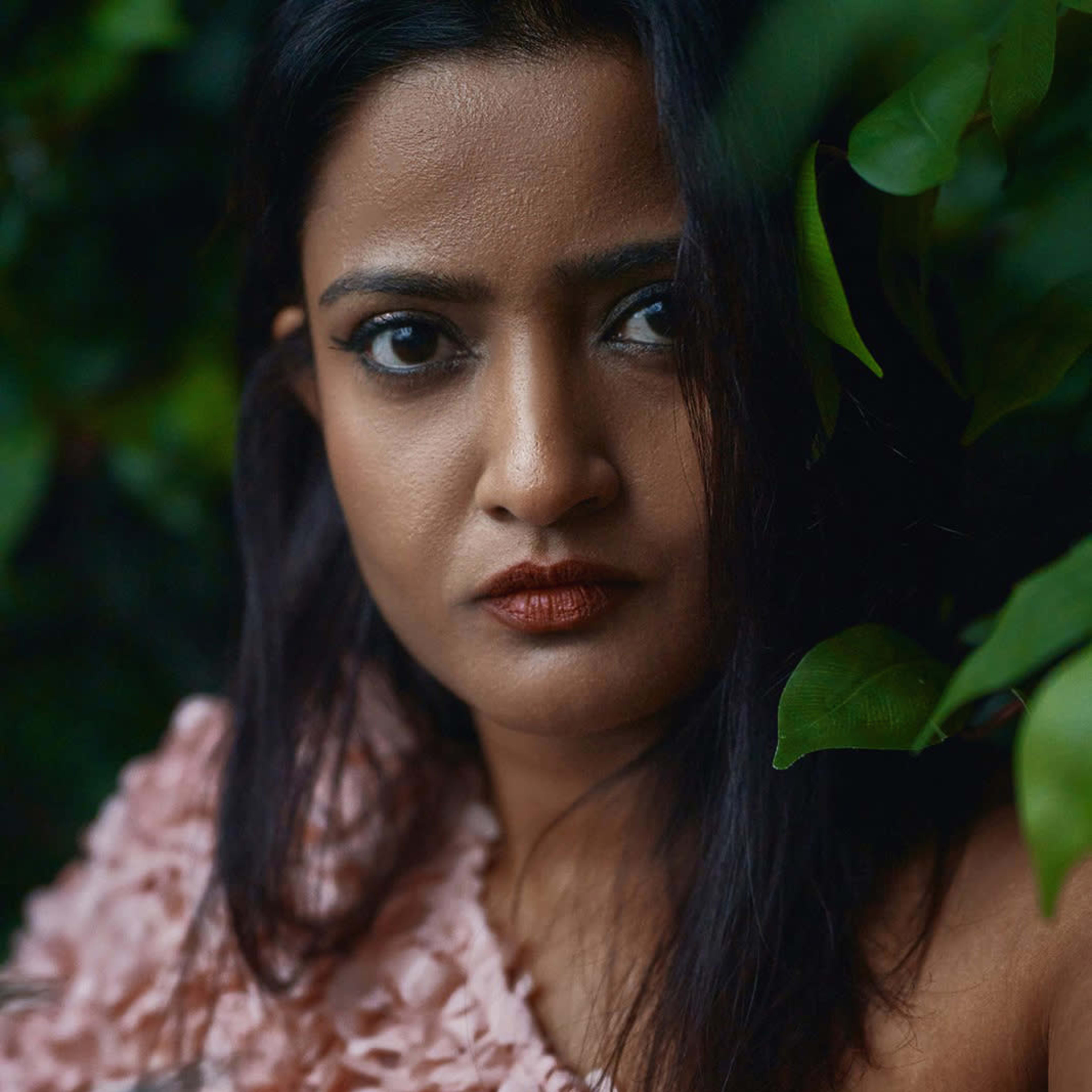 A person with dark hair poses in front of a green wall, wearing a textured pink garment.
