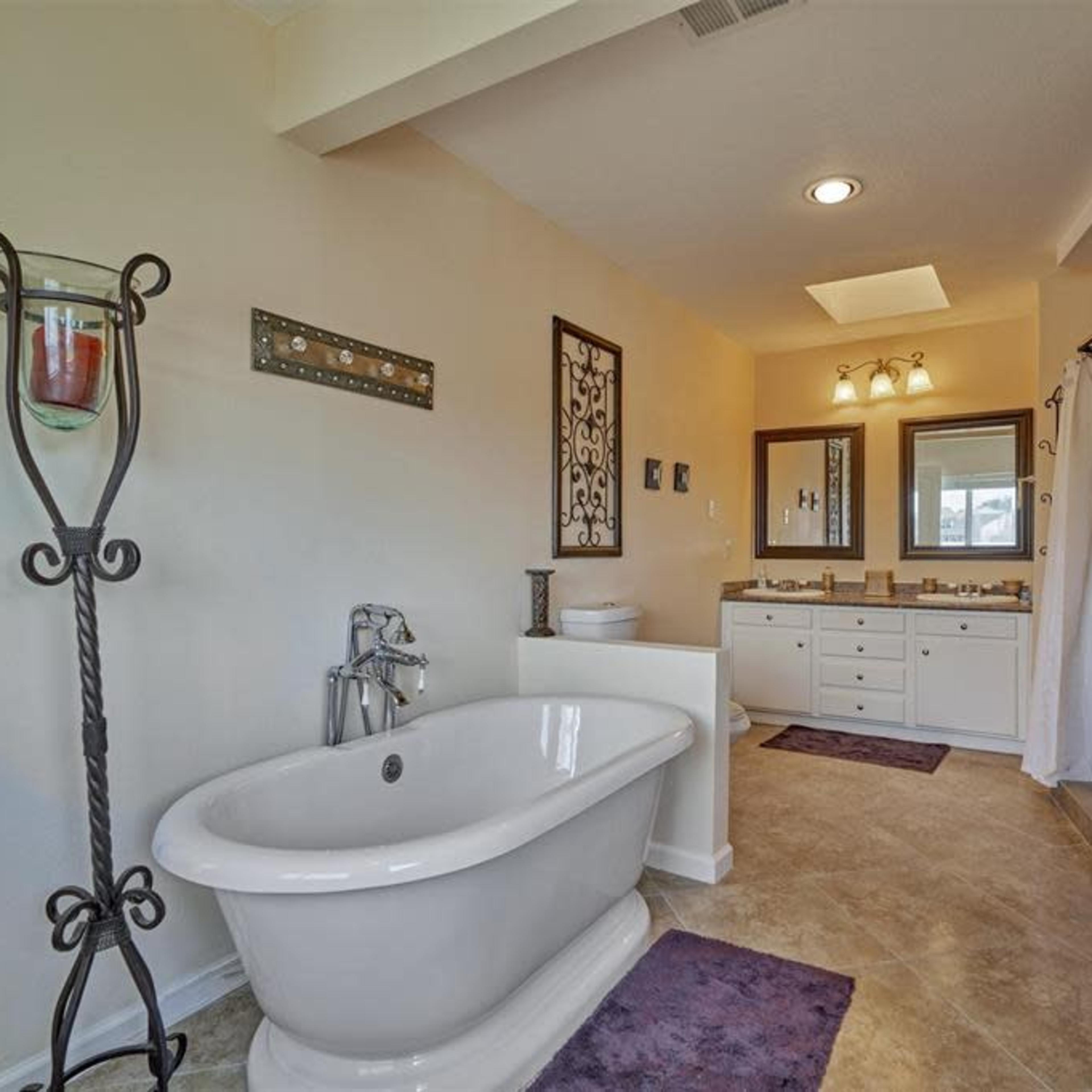 A spacious bathroom features a freestanding bathtub, double vanity with mirrors, and neutral-colored walls.