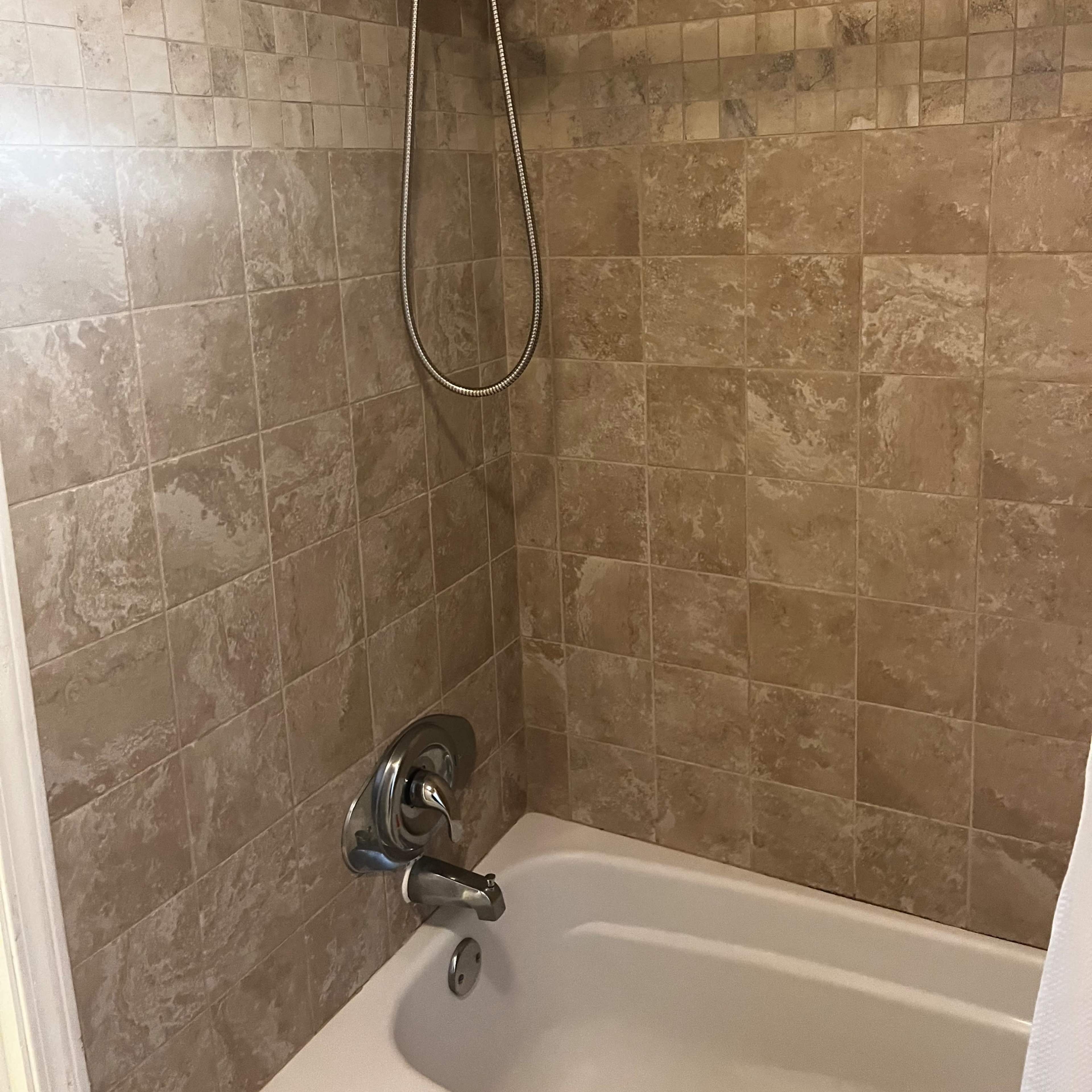 A shower and bathtub combination with tiled walls in neutral tones.
