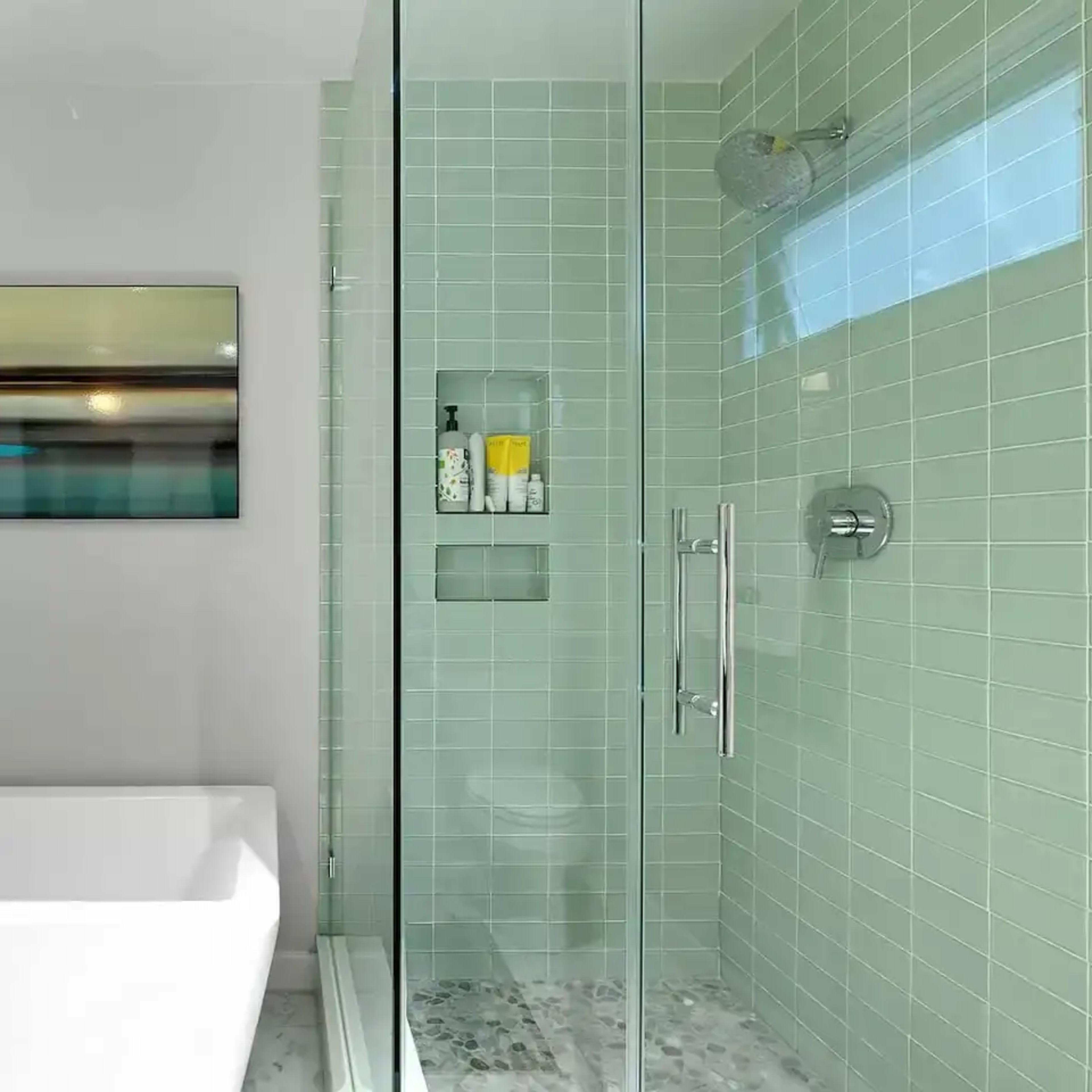 A modern bathroom featuring a freestanding white bathtub and a glass-enclosed shower with green tiled walls.