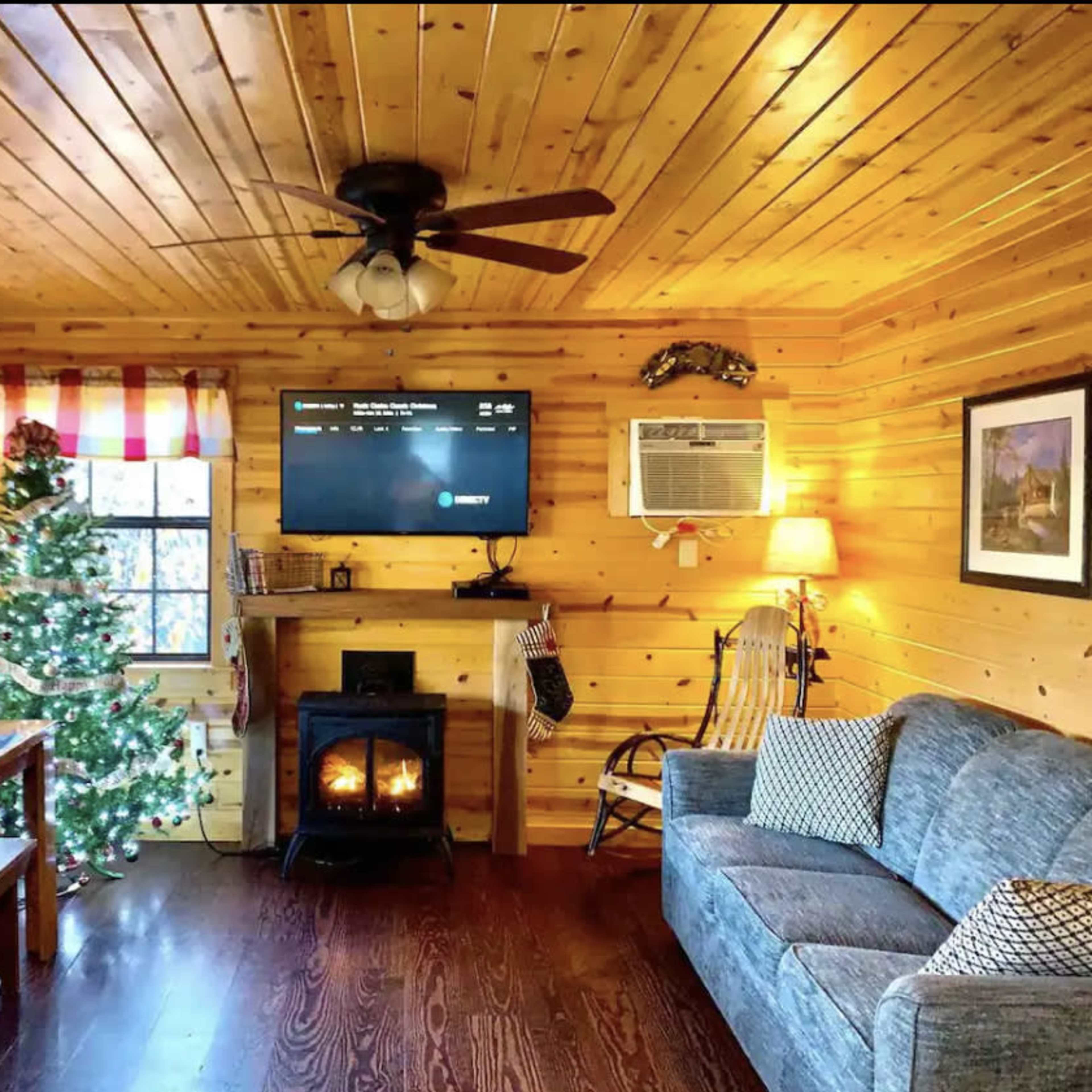A cozy living room features wooden walls, a Christmas tree, a fireplace, and a couch.