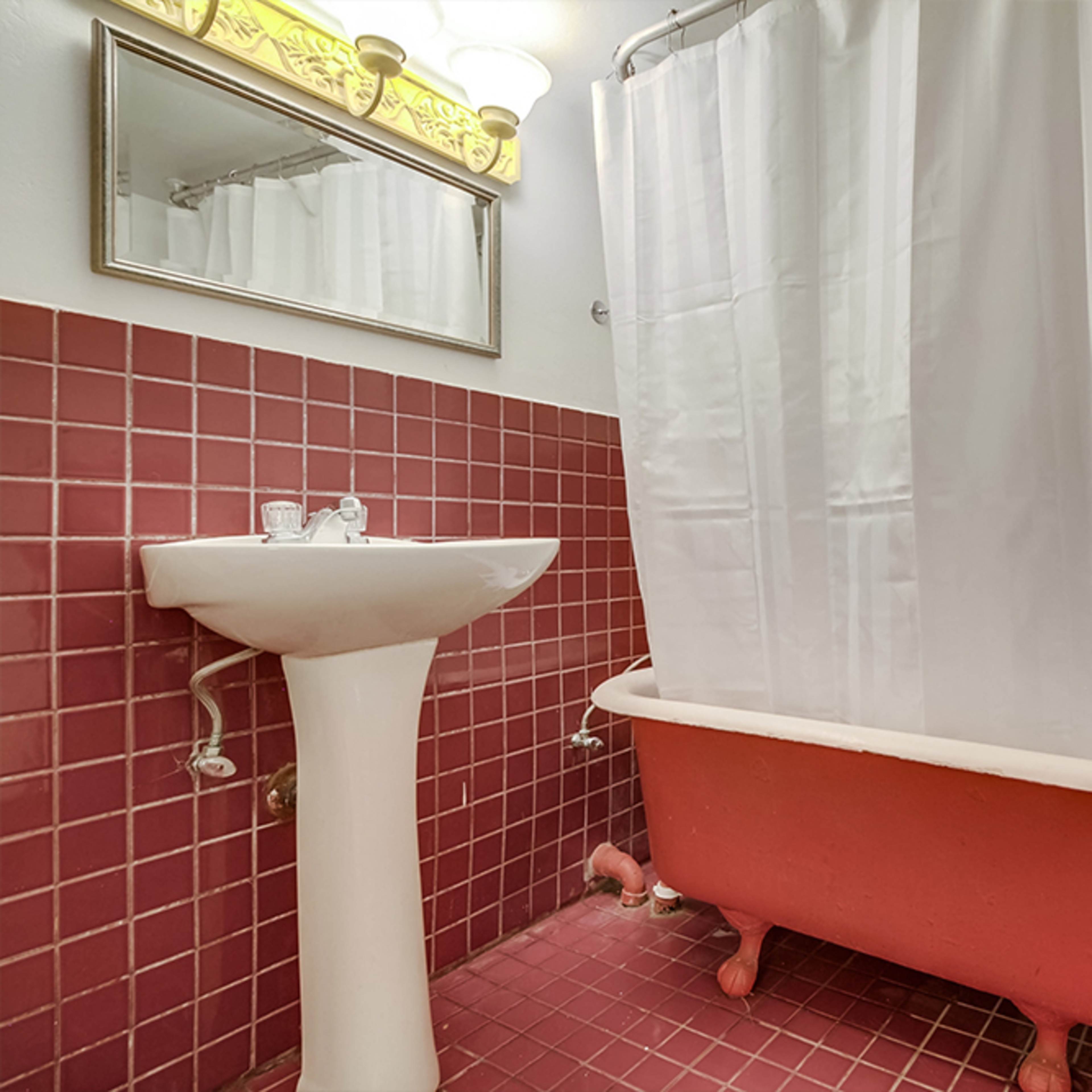 A small bathroom featuring a pink tiled floor, a white shower curtain covering a bathtub, and a pedestal sink.