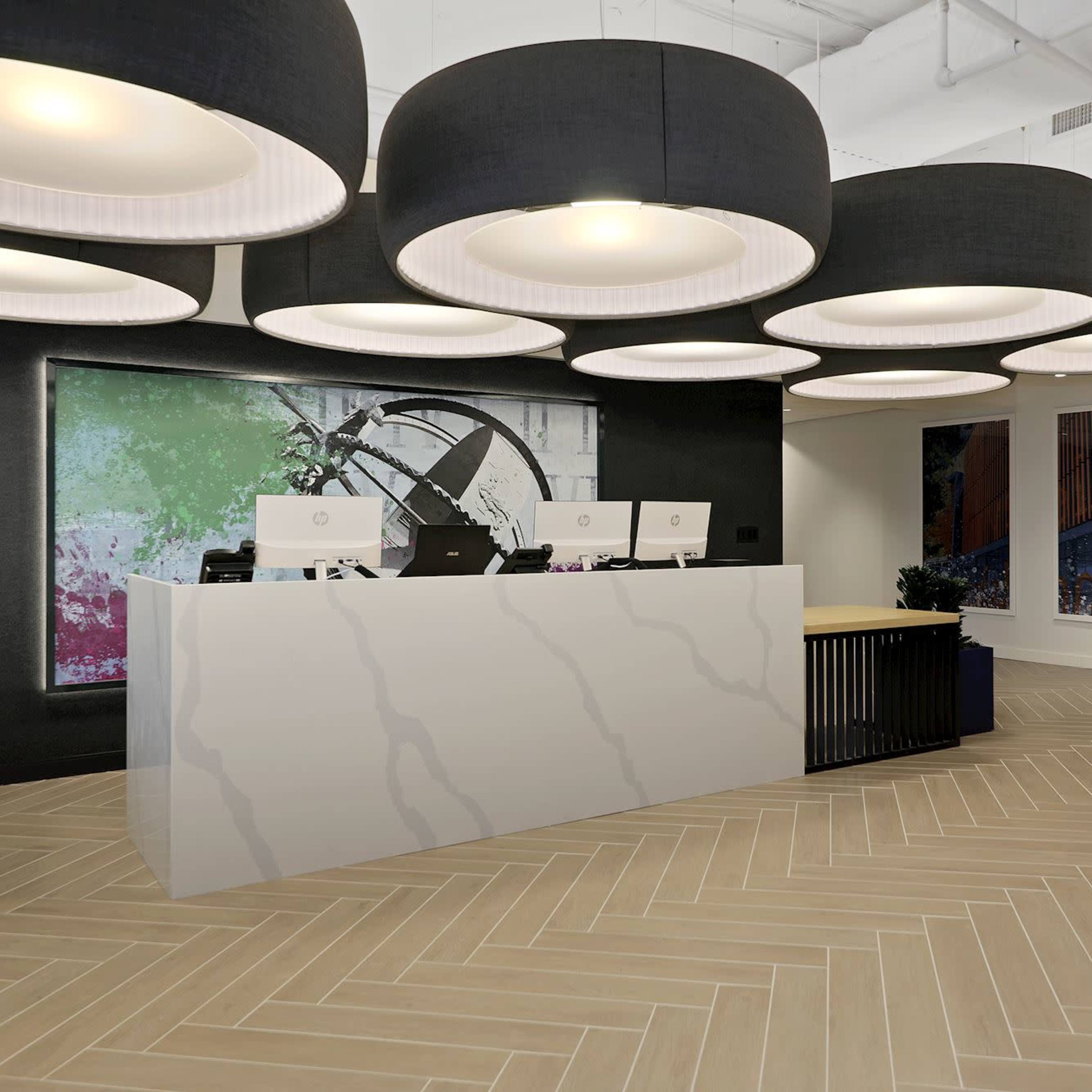 A modern reception area features a white marble front desk with multiple computer stations, surrounded by large black pendant lights and colorful abstract artwork on the walls.