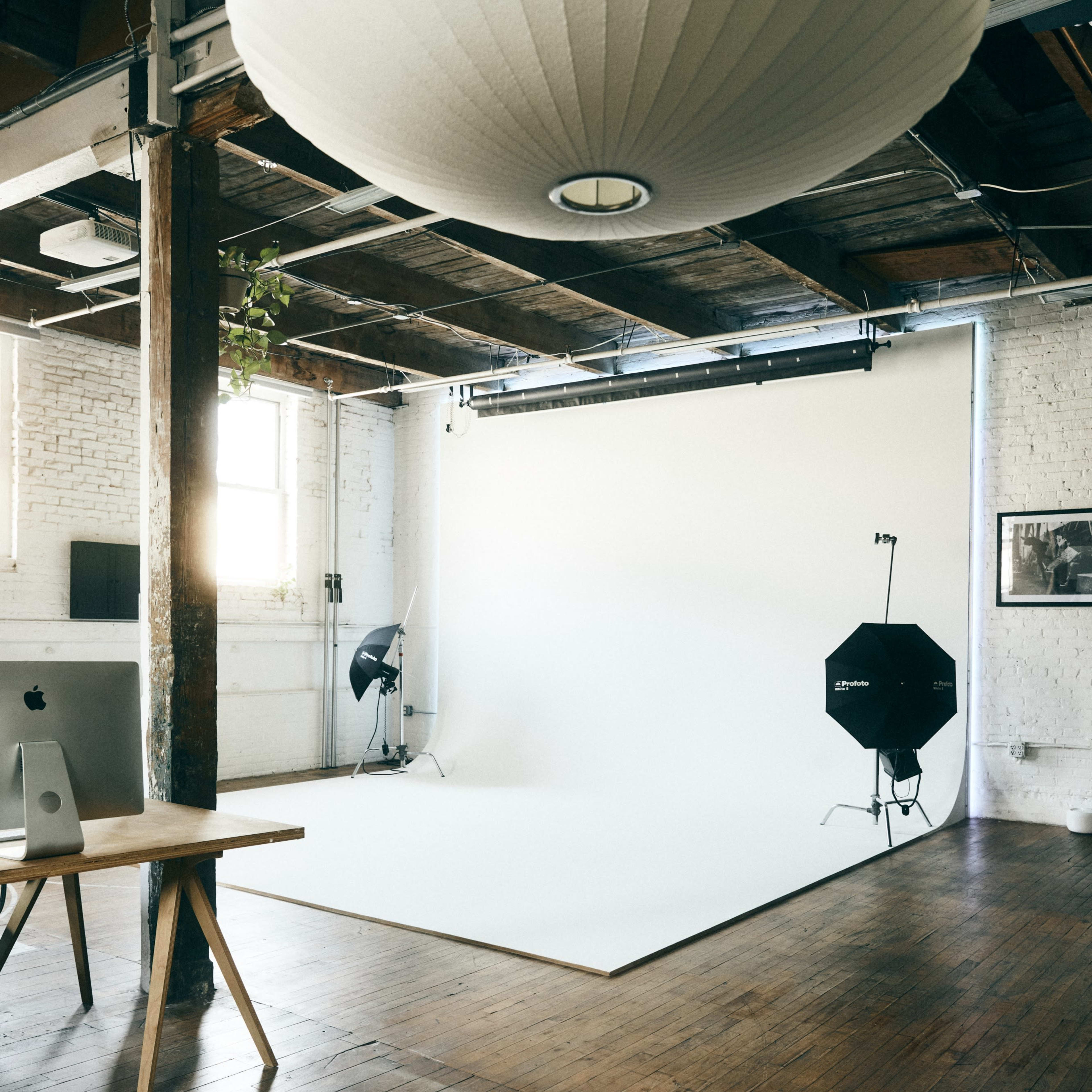 A spacious photography studio with a white backdrop, soft lighting, and wooden flooring.