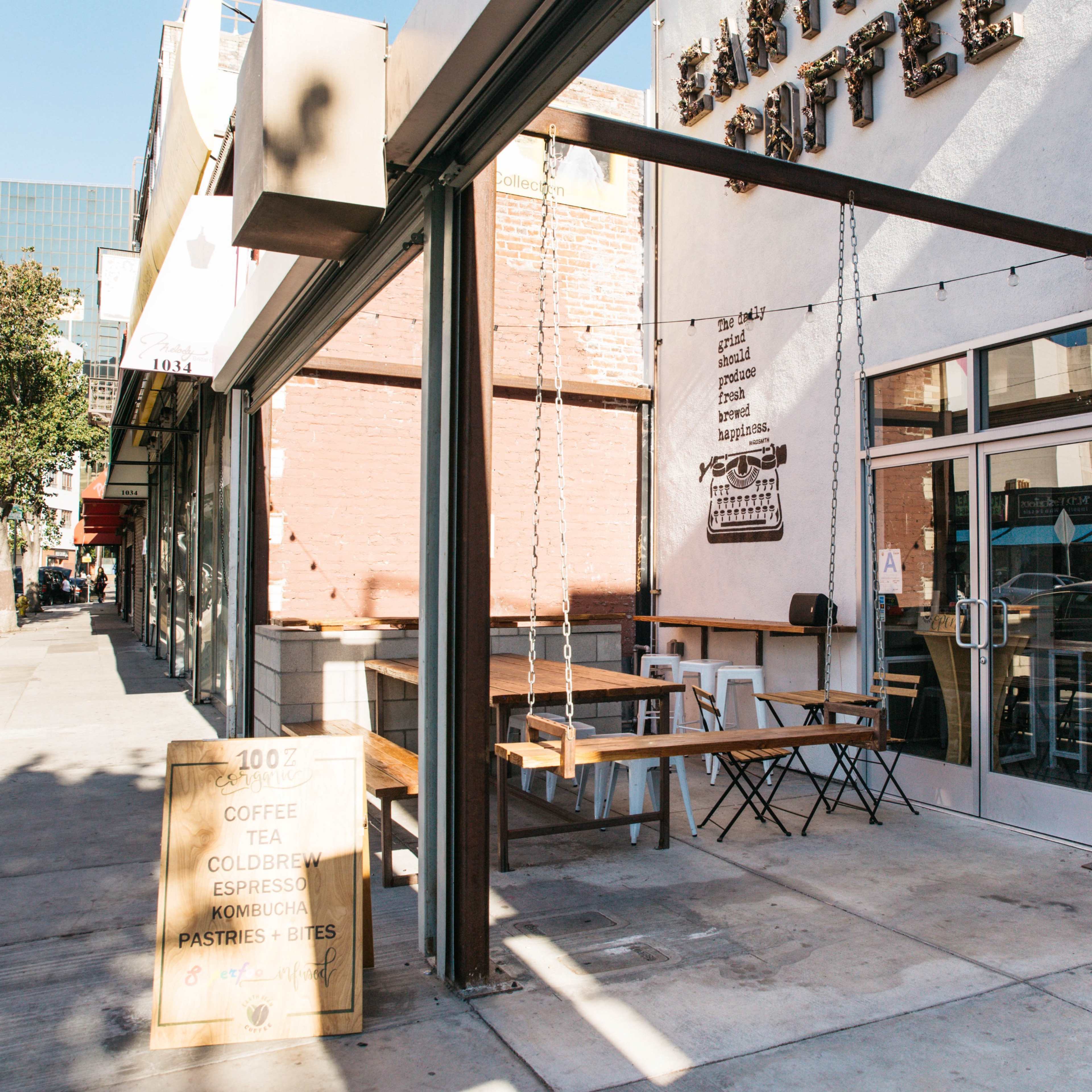 A coffee shop with outdoor seating and a sign displaying menu items is located on a sidewalk in a city.