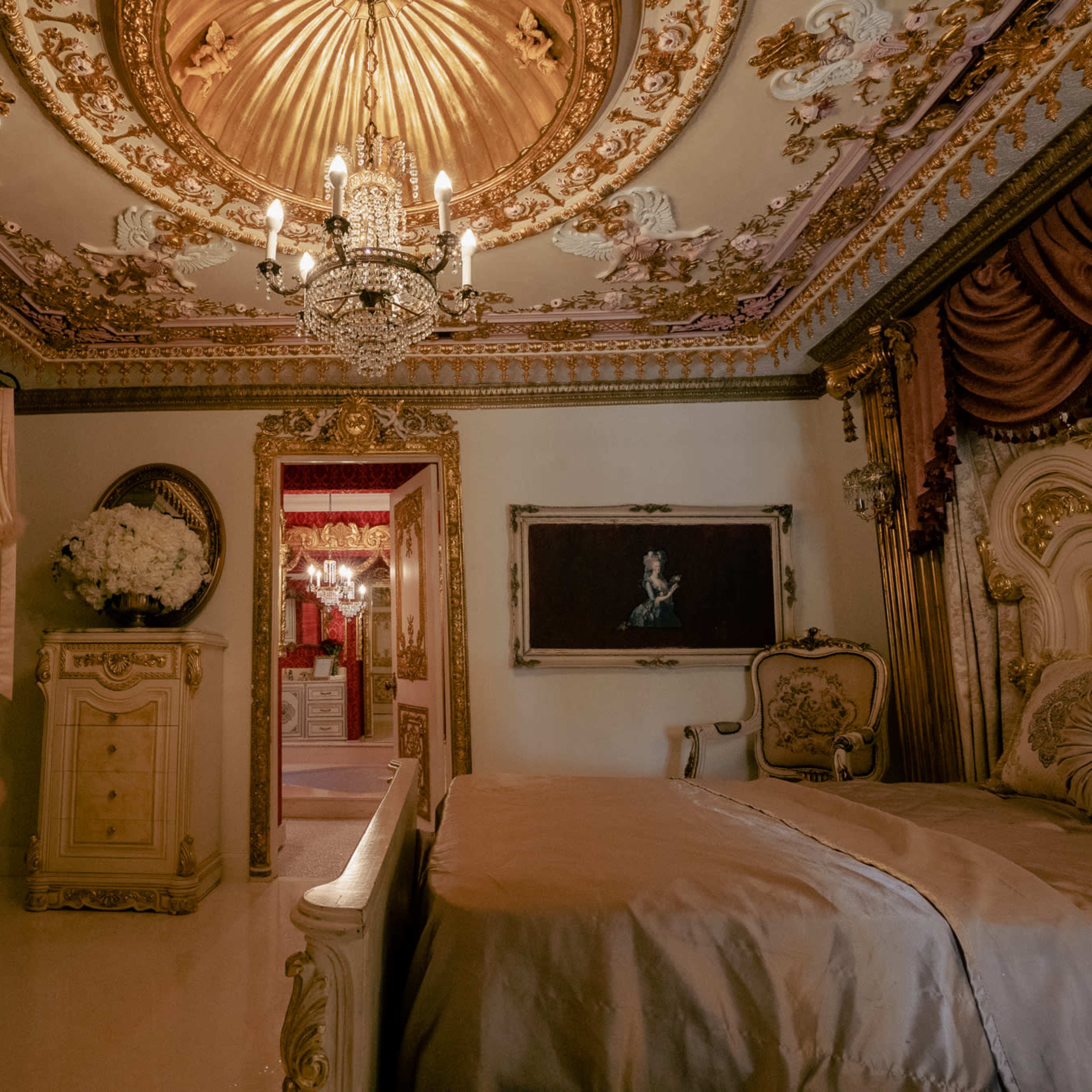 A lavishly decorated bedroom with ornate golden ceilings, a crystal chandelier, and luxurious furnishings.