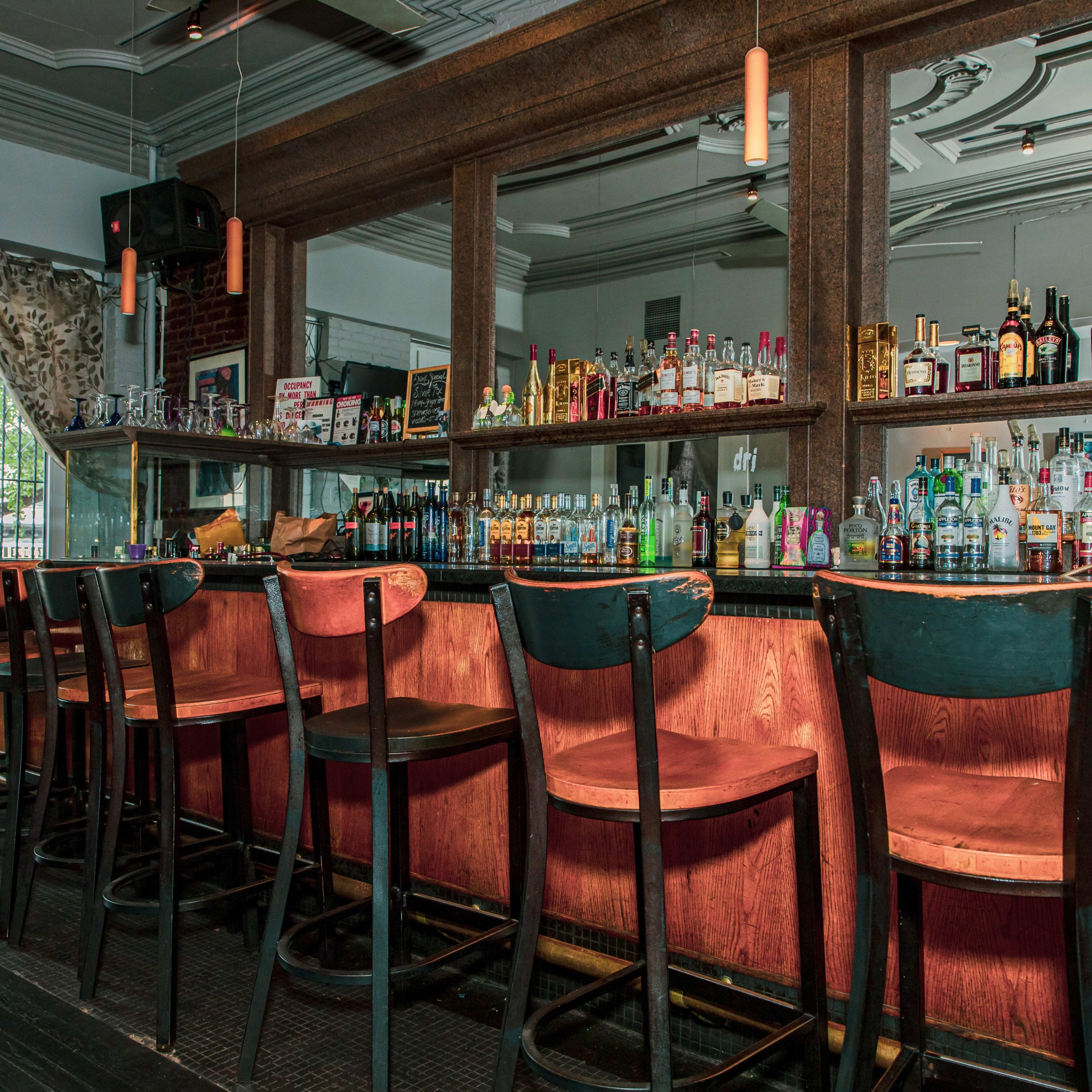A well-lit bar with wooden stools lined up in front of a counter filled with various bottles of liquor.