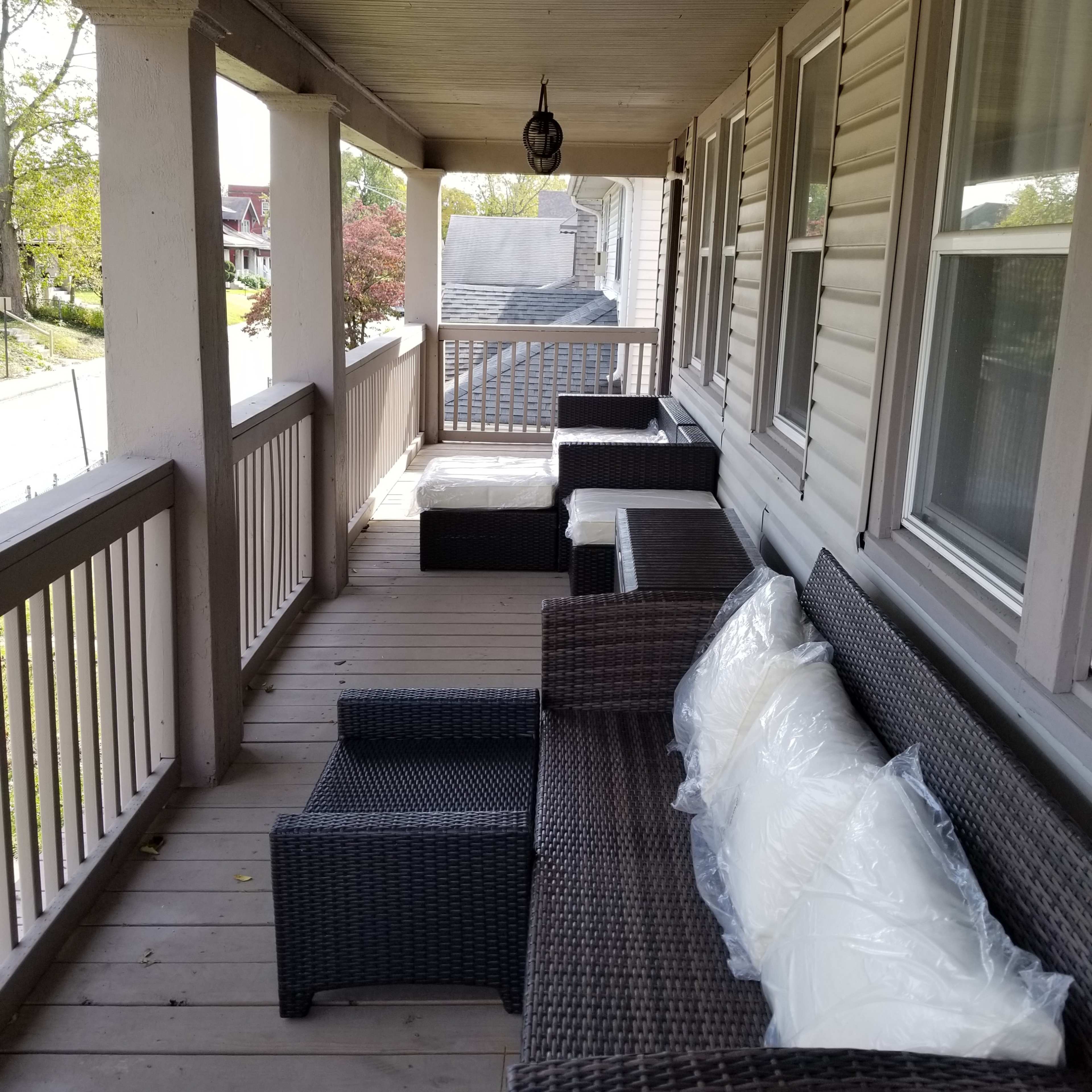 A covered porch with wicker seating arrangements and white cushions.