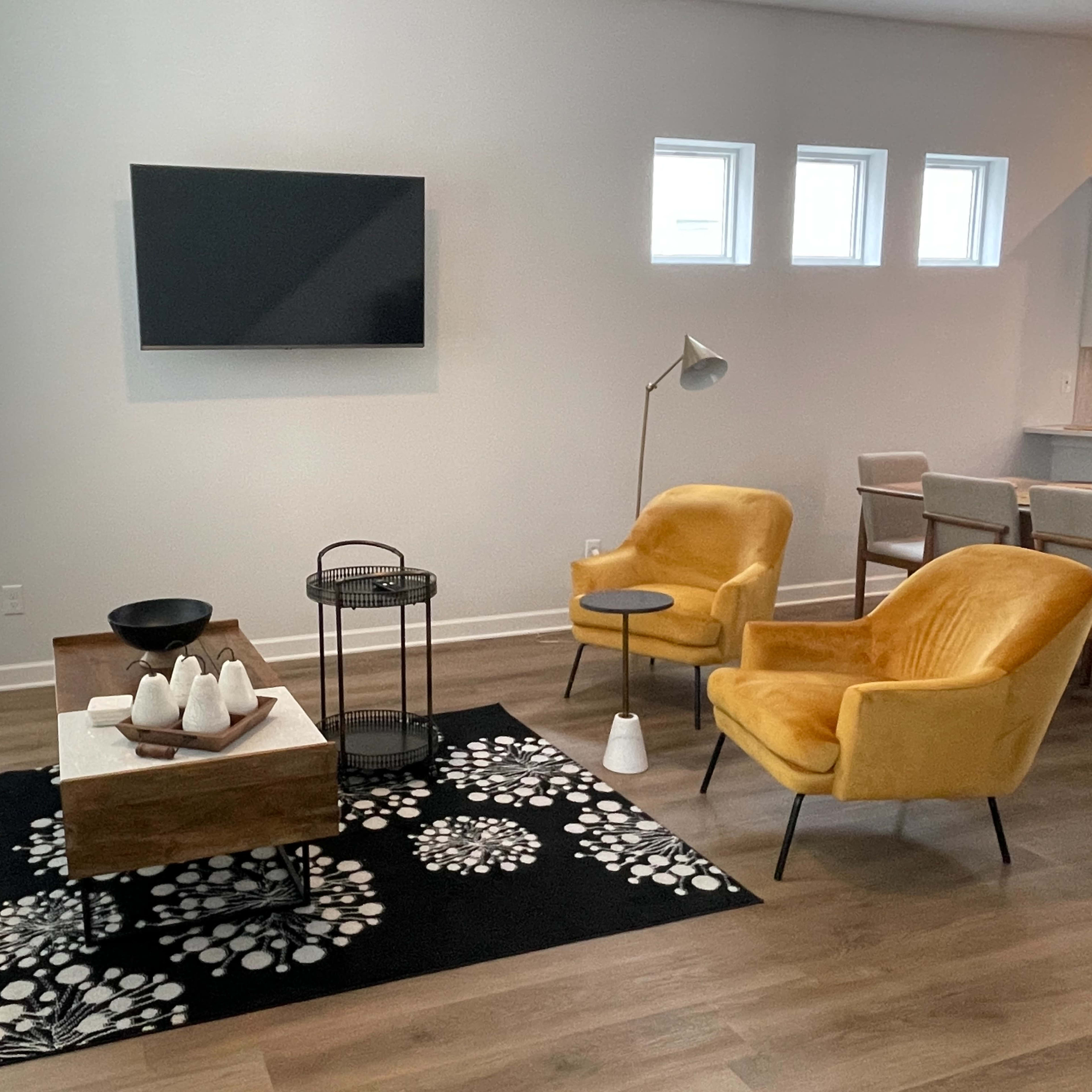 The living room features a gray sofa, two yellow armchairs, a wooden coffee table with decorative items, and a television mounted on the wall.