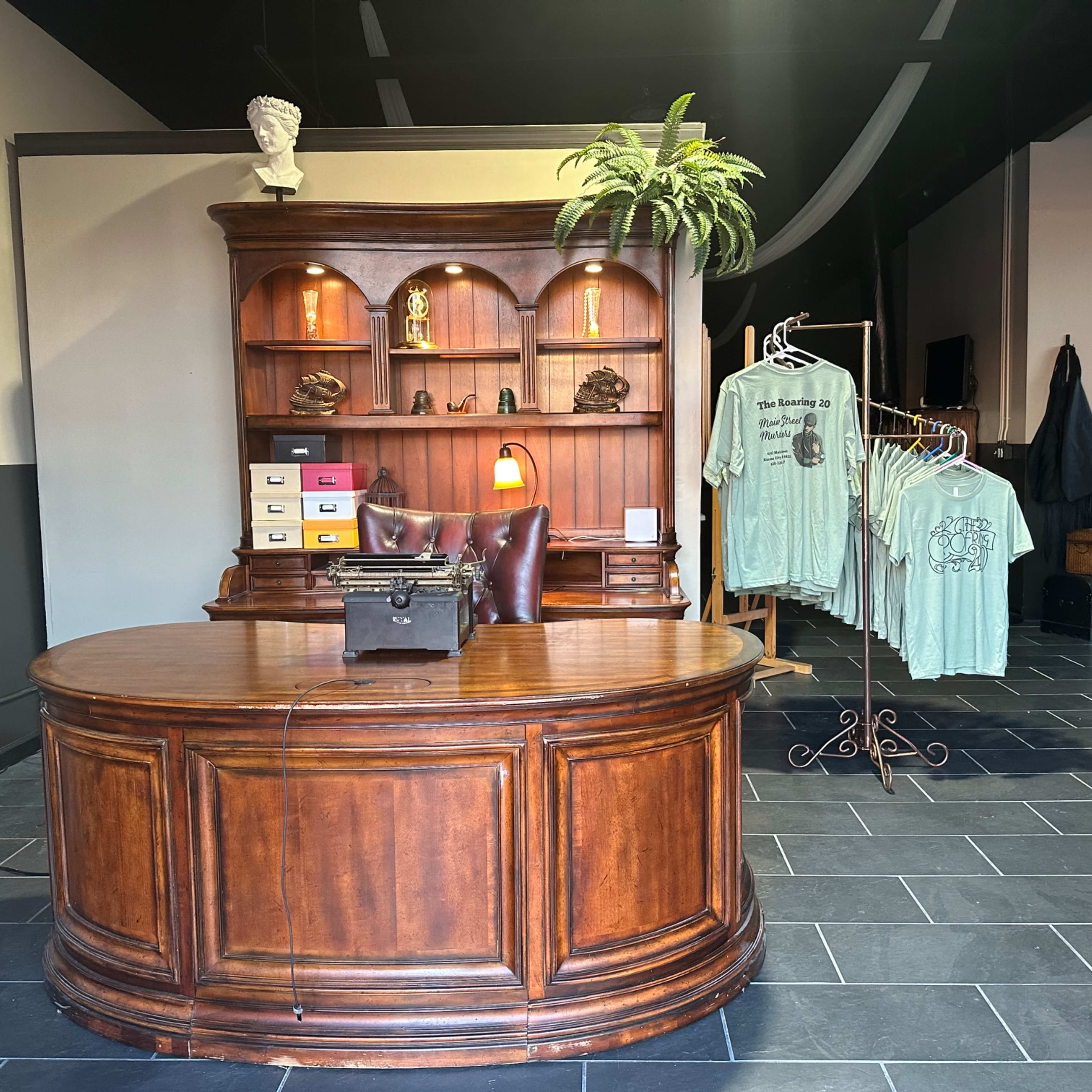A wooden reception desk with a vintage typewriter and shelves above it, alongside a rack of T-shirts displayed in a well-lit space.
