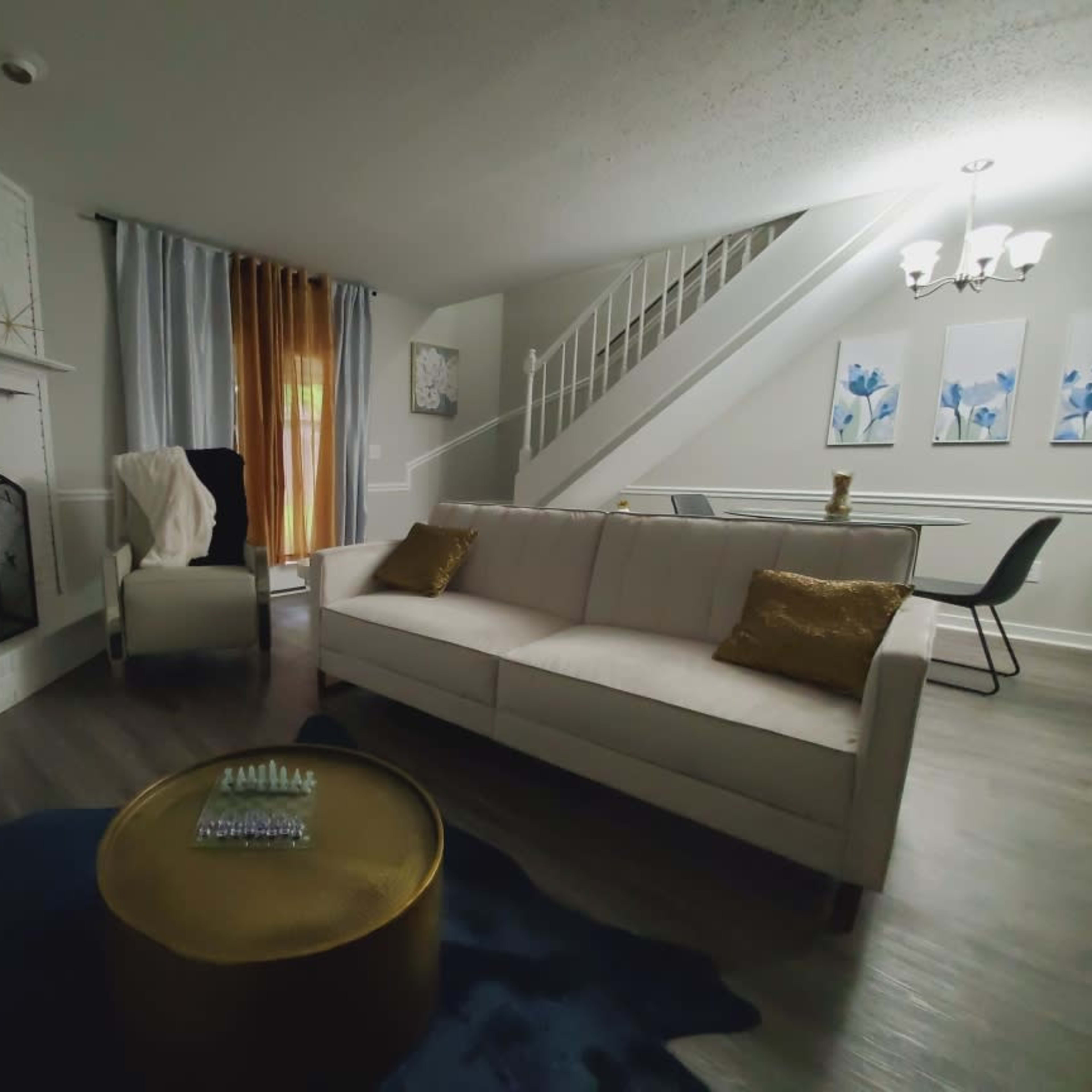 A modern living room with a white couch, a decorative gold coffee table, a fireplace, and a staircase in the background.