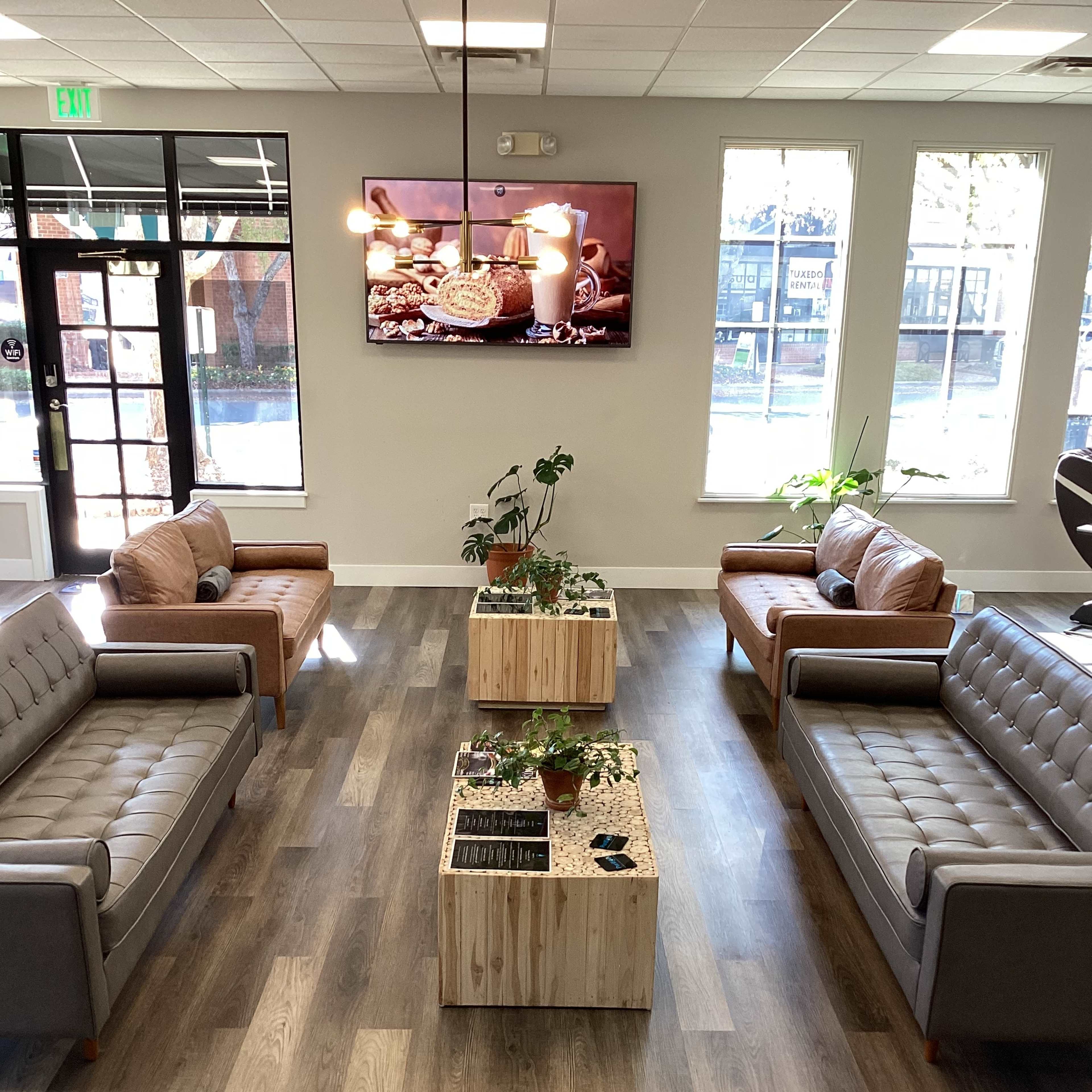 A modern lounge area with two sets of sofas facing each other and a wooden coffee table in the center, all under a television displaying a food-themed video.