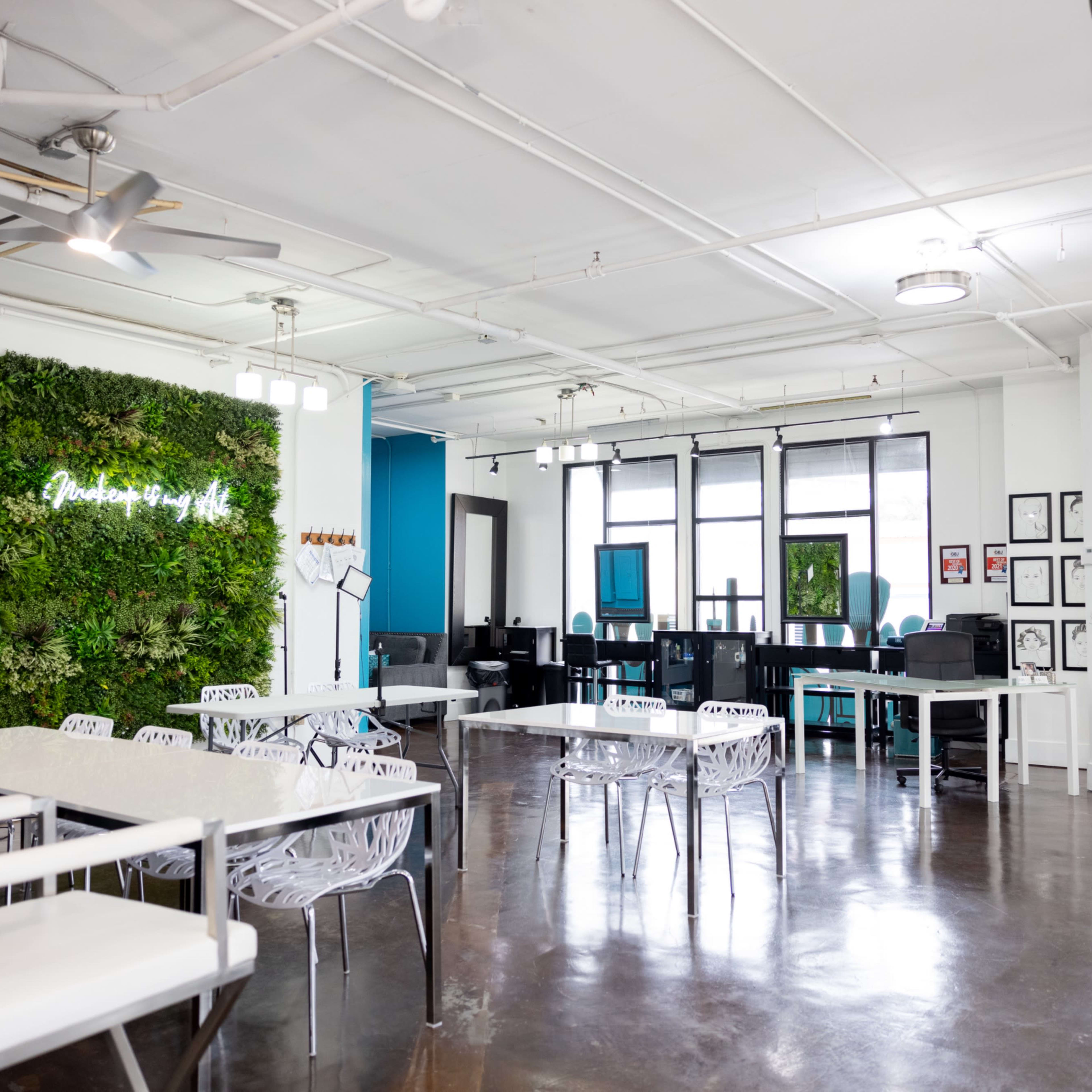 A modern, open workspace featuring a green wall, white furniture, and several workstations with computers.
