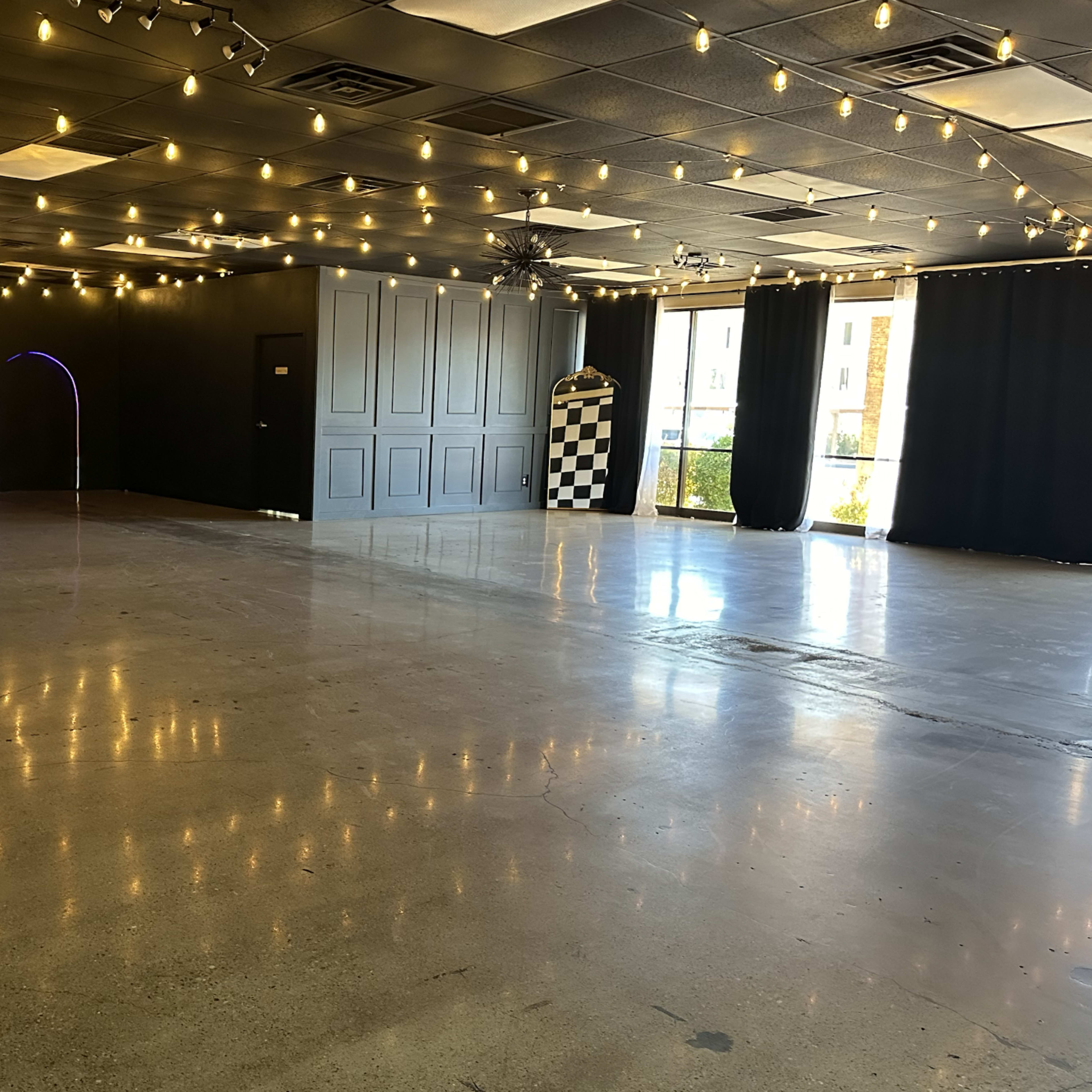 An empty event space with polished concrete floors, decorative string lights overhead, and colorful arches in the walls.