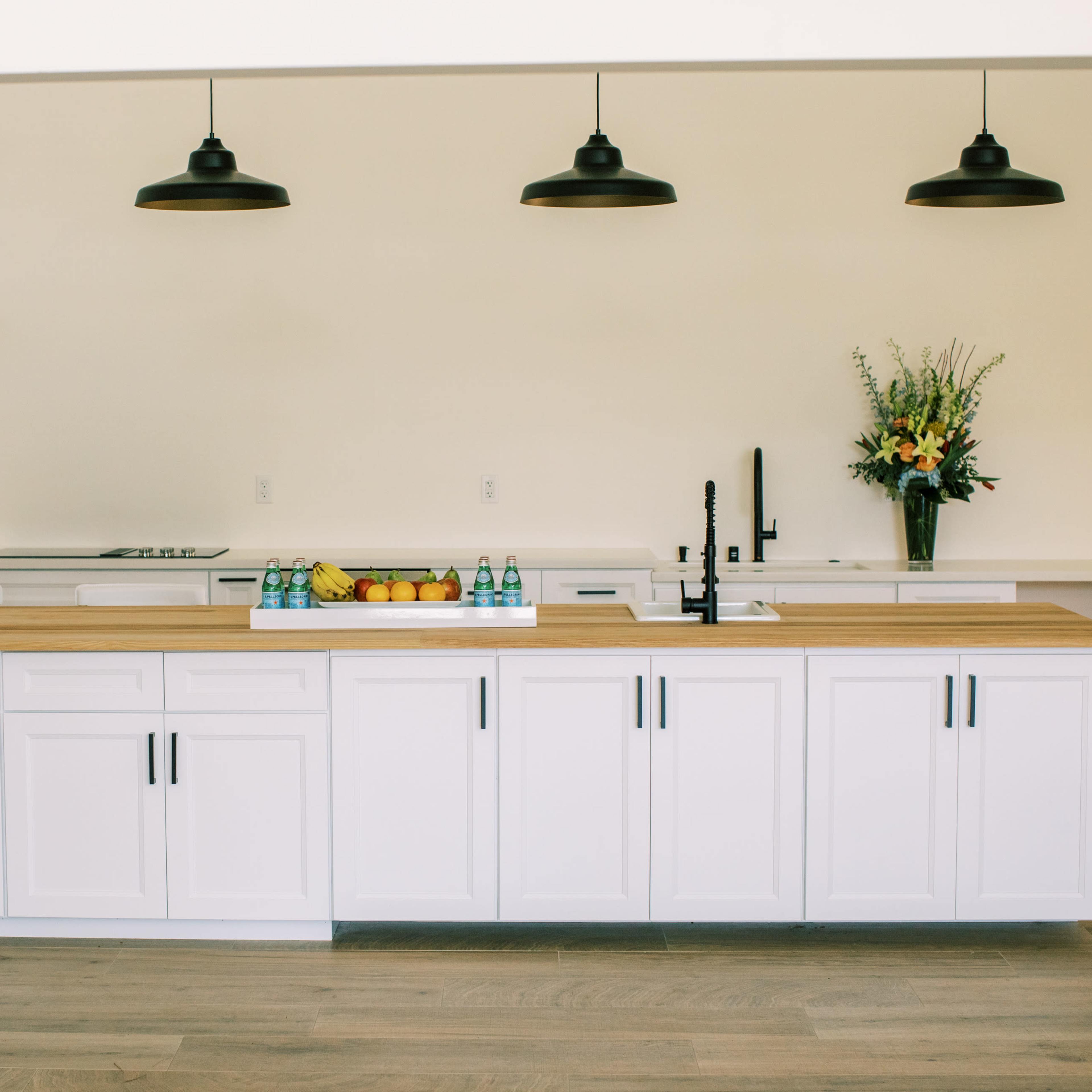 A modern kitchen with a central wooden island, white cabinetry, and three black pendant lights.
