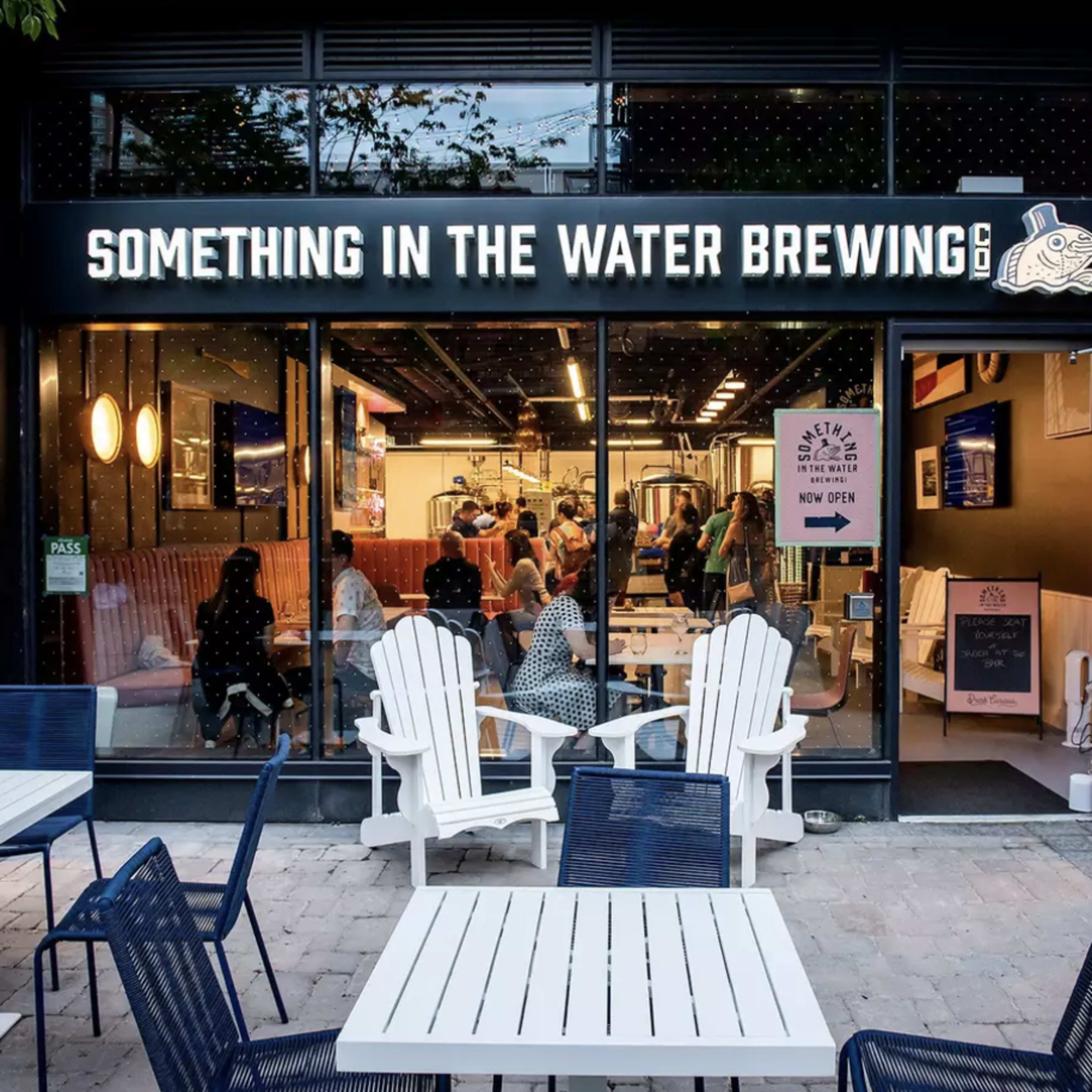 The exterior of "Something in the Water Brewing" features a welcoming entrance with outdoor seating and patrons visible inside.