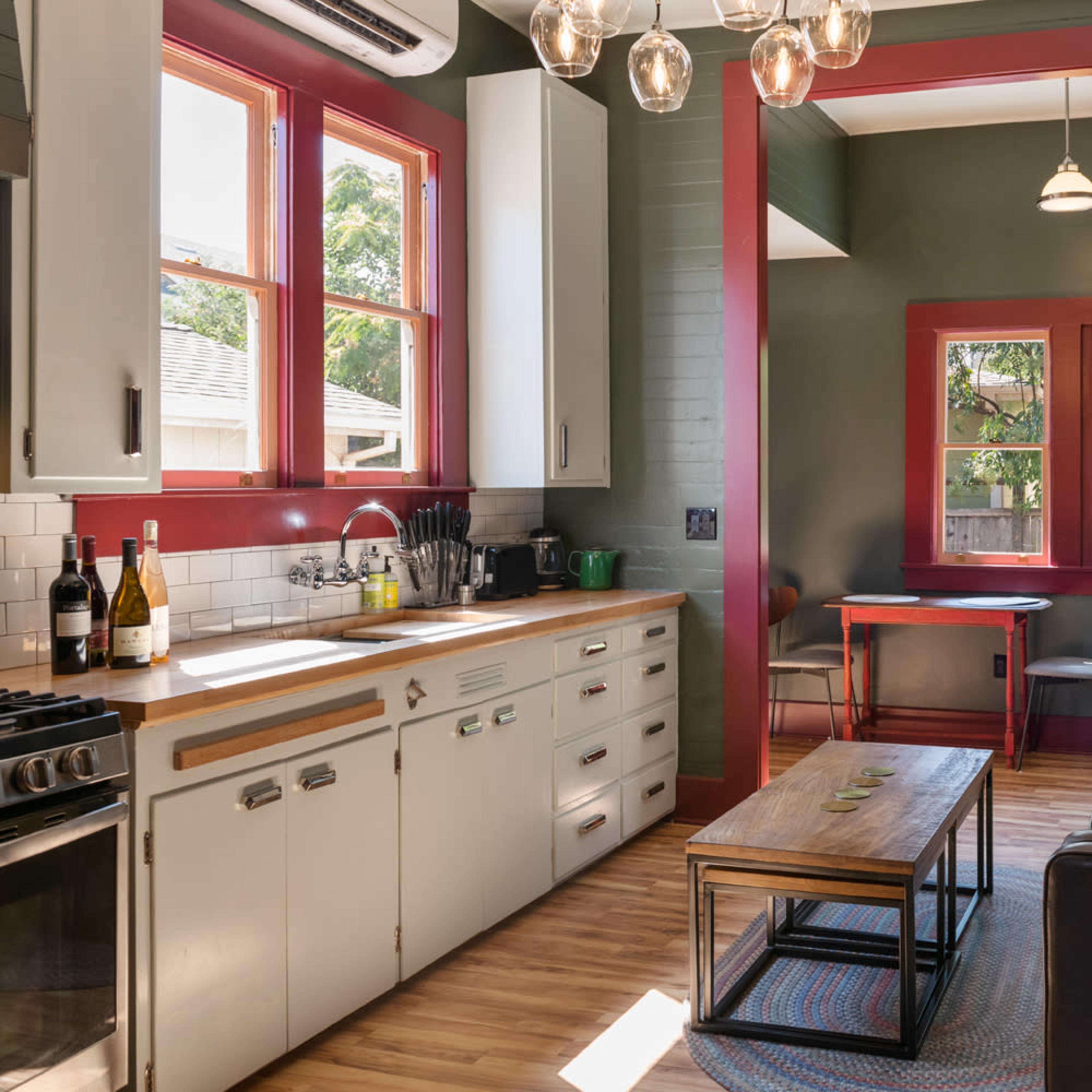 A modern kitchen with white cabinets and a wooden dining area adjacent to a cozy living space featuring a leather sofa and a coffee table.