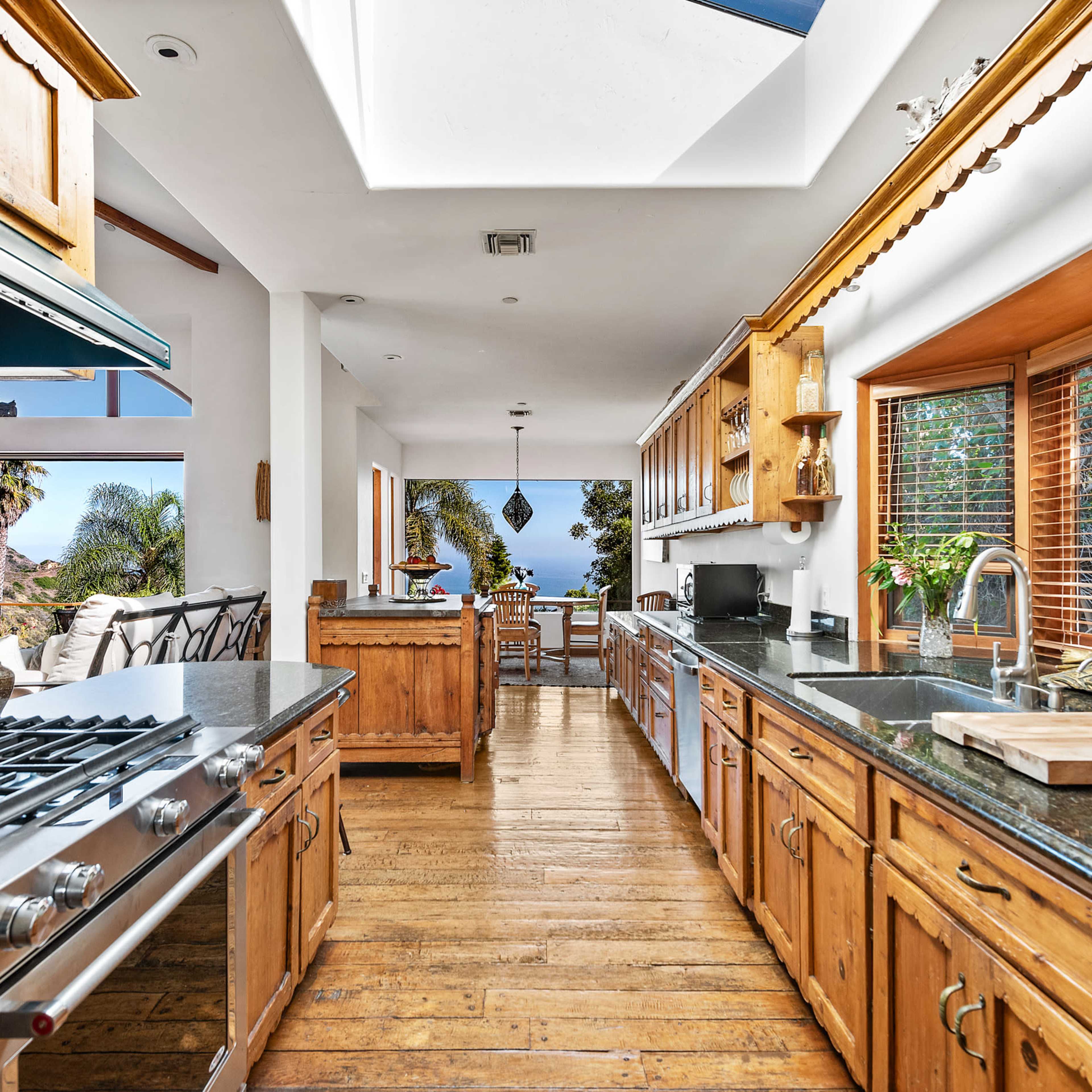 A spacious kitchen with wooden cabinets, a large island, and large windows that provide a view of the outdoors.