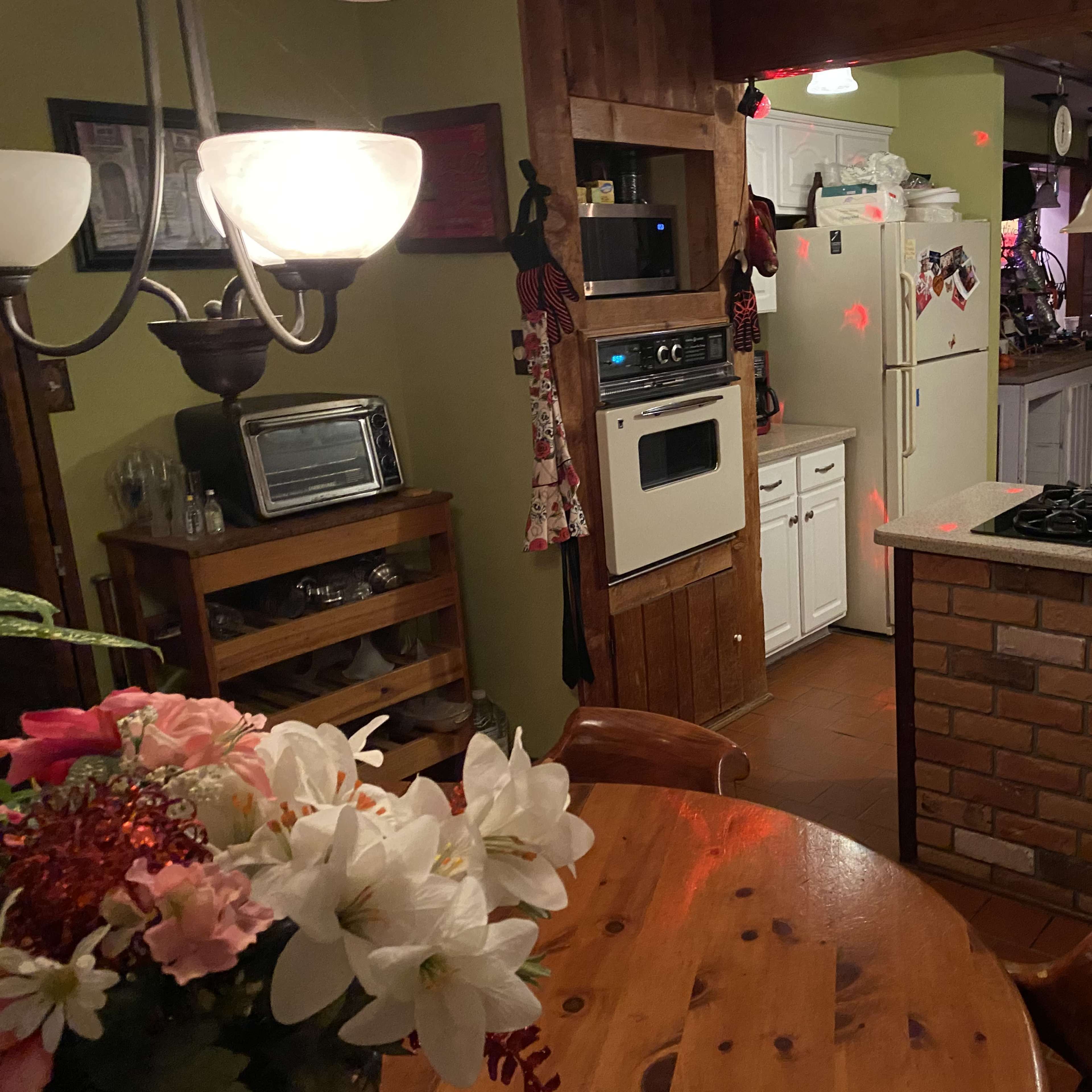 A kitchen with wooden accents, a round table with flowers, and various appliances, including a stove and a refrigerator.