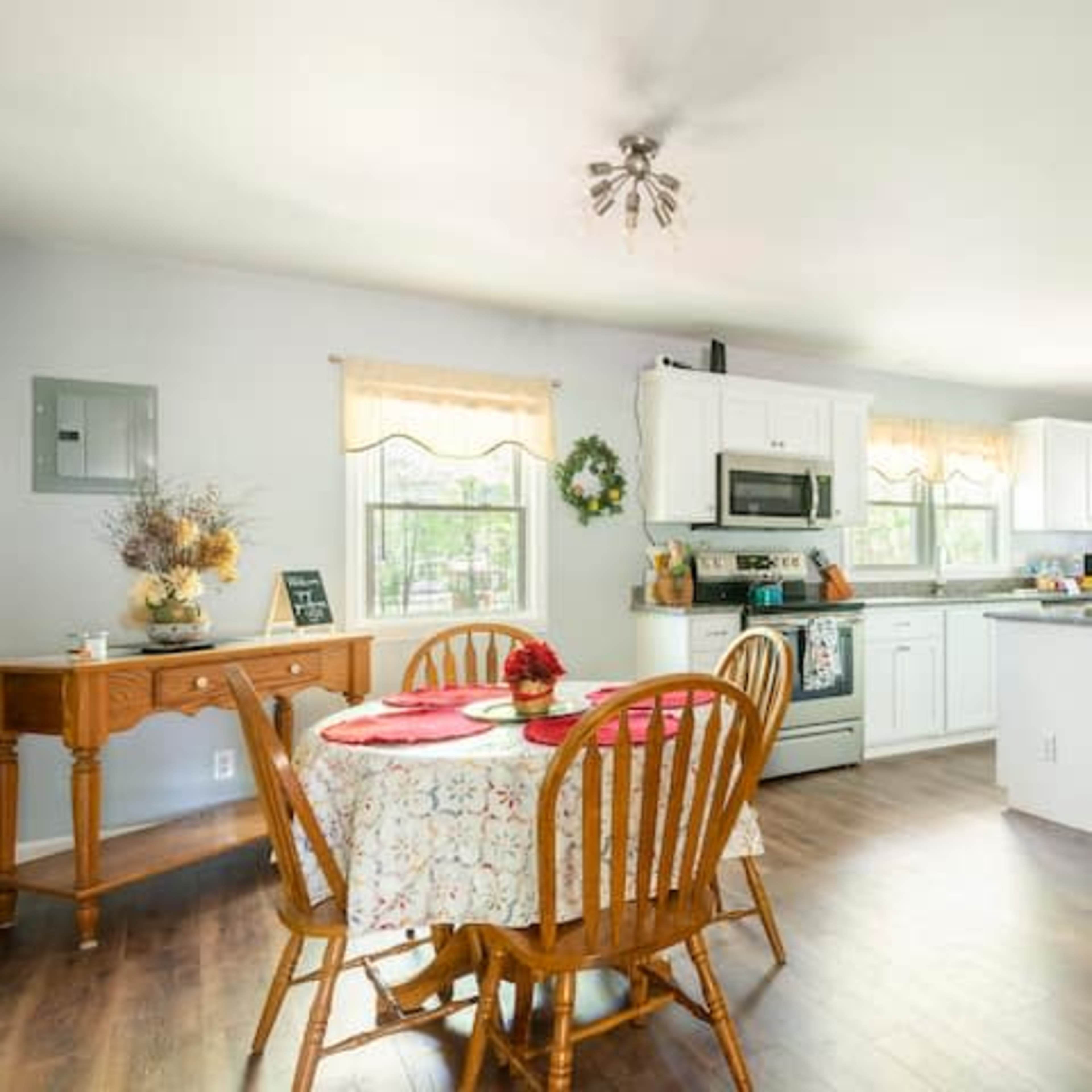 A kitchen features a dining area with a round table, wooden chairs, and a counterspace equipped with modern appliances and light-colored cabinetry.