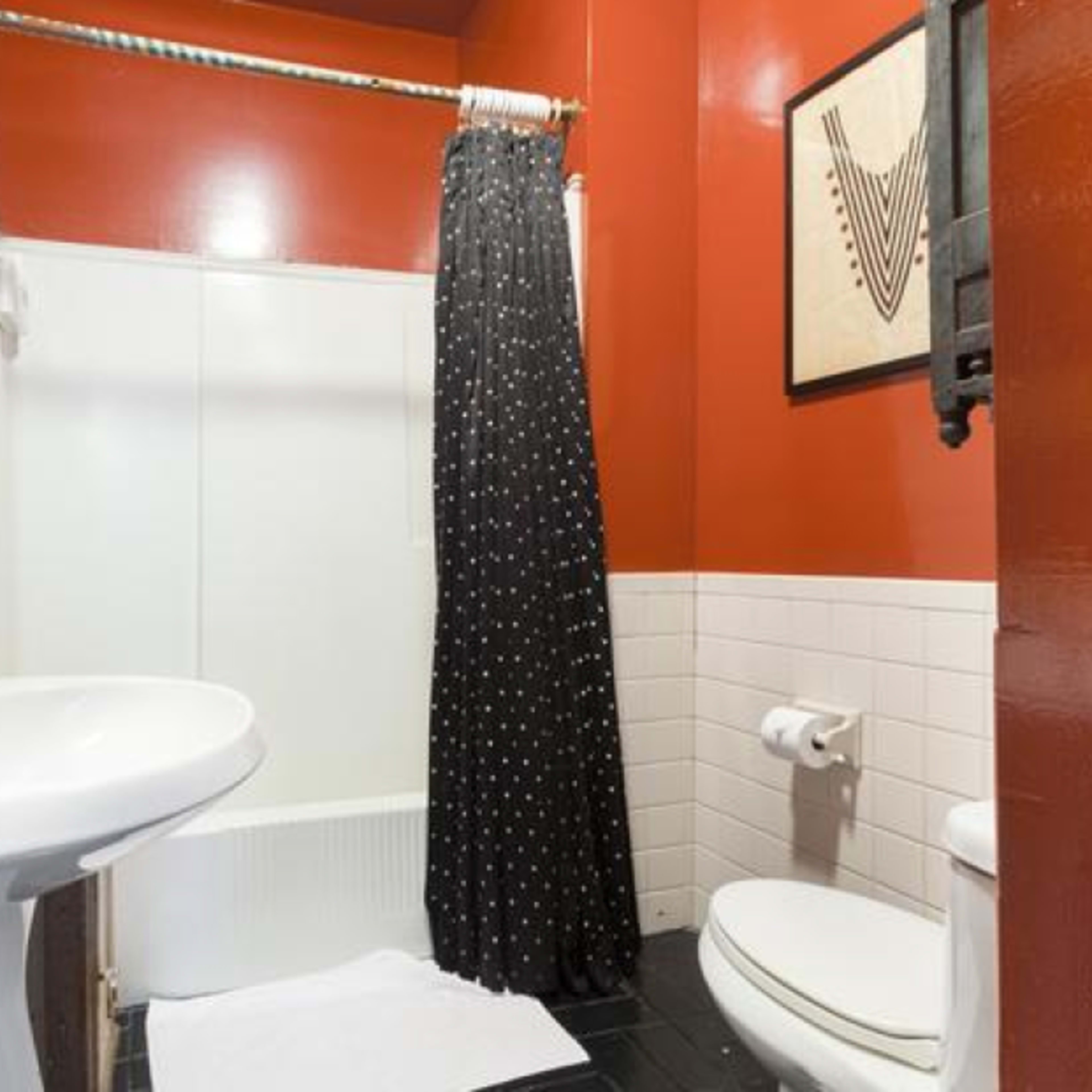 A small bathroom featuring a white shower stall, a pedestal sink, a toilet, and a black polka dot shower curtain, with red walls and white tiled accents.