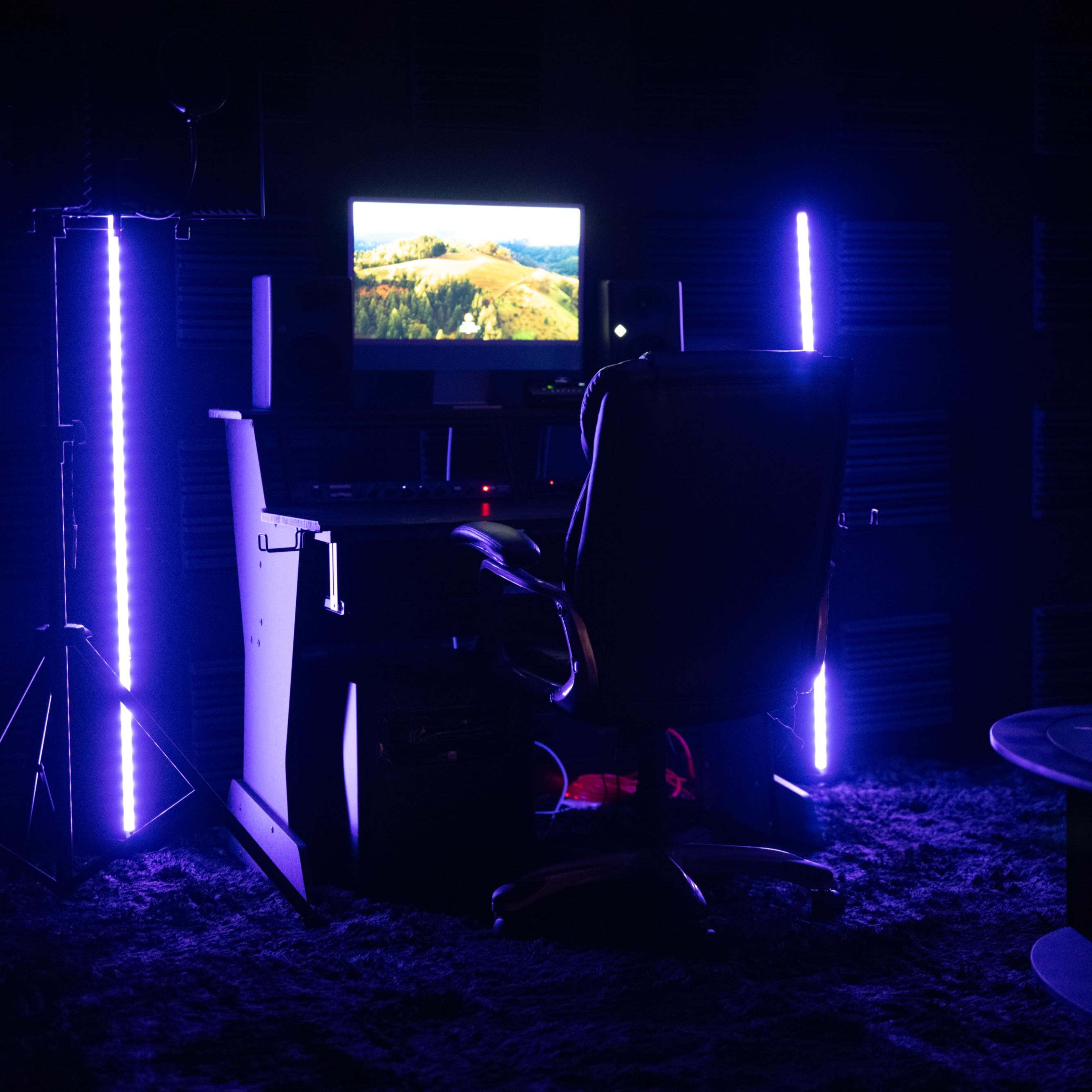A dimly lit room features a desk with a computer monitor, an office chair, and a pink couch beside a glass coffee table.
