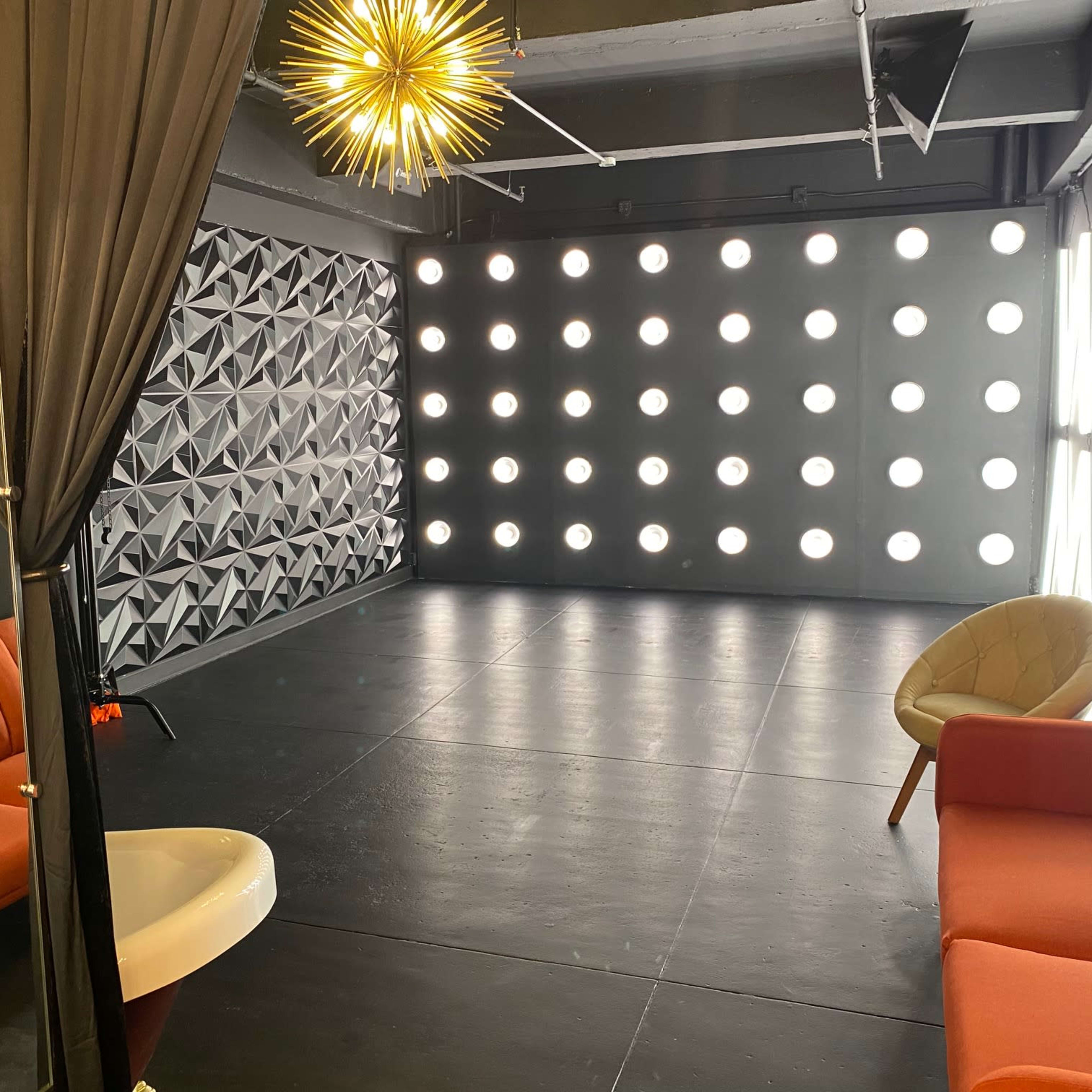 A modern studio space with a geometric wall design, bright lighting, and two orange sofas.