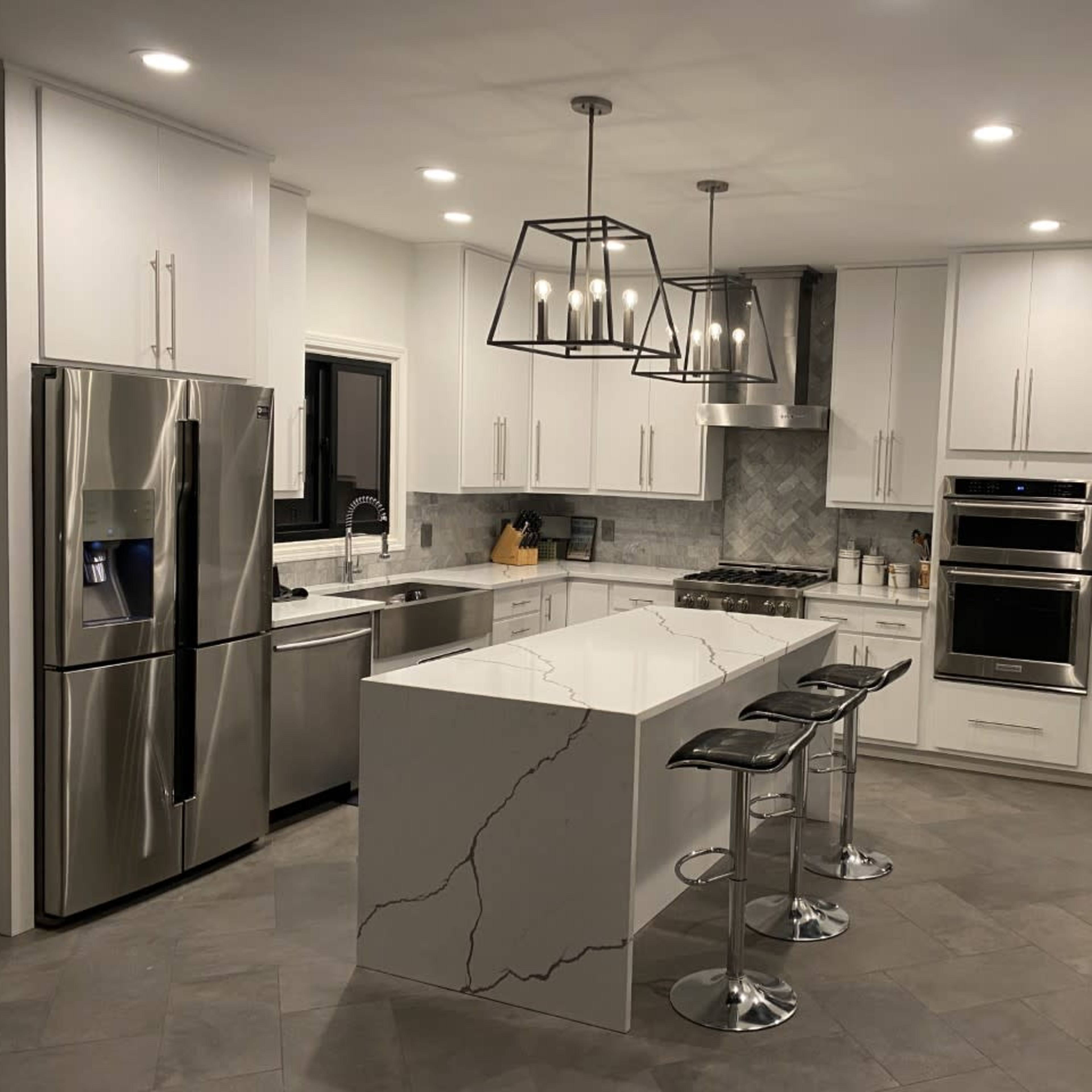 A modern kitchen featuring white cabinets, stainless steel appliances, a large island with a marble countertop, and pendant lighting.